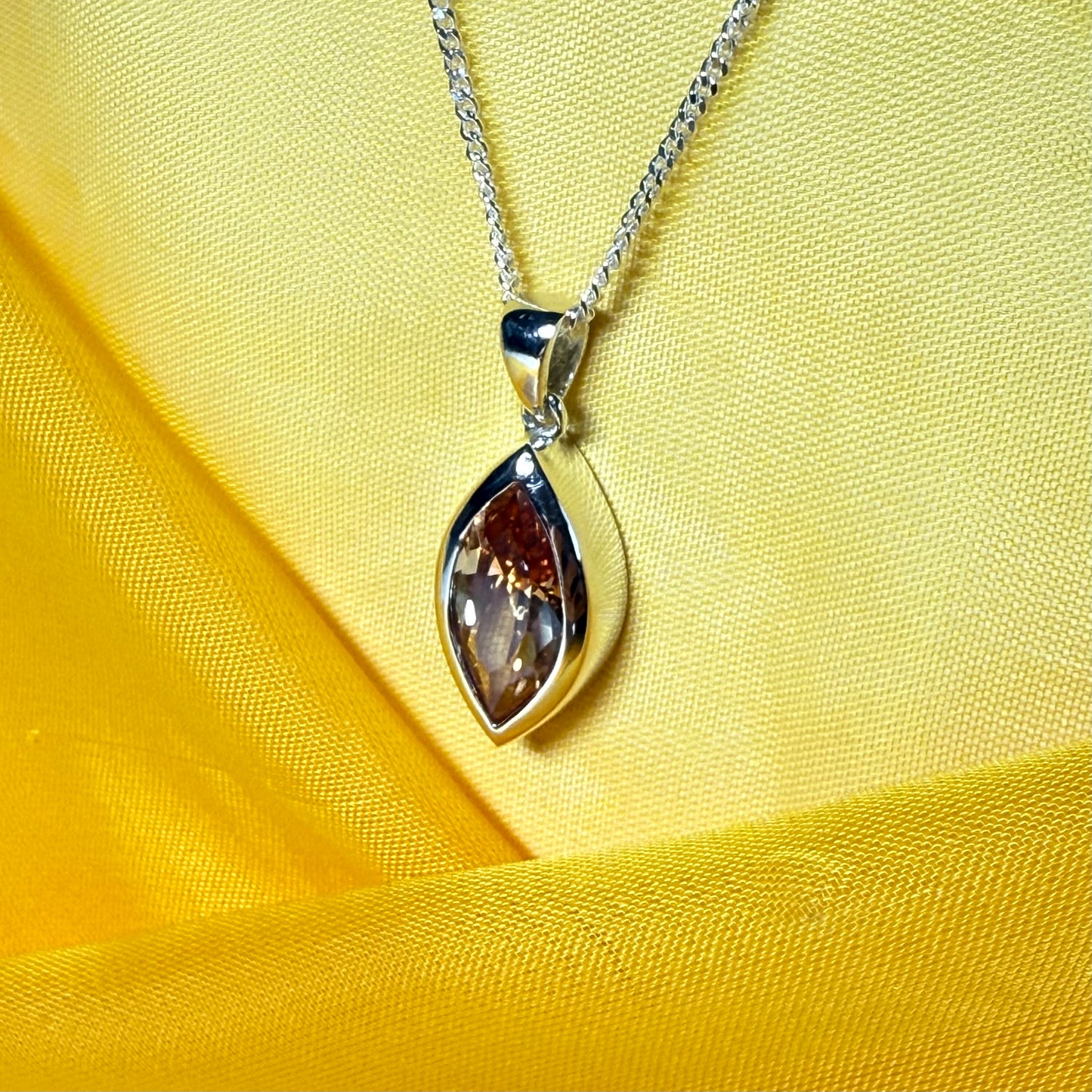 Silver pendant necklace with a marquise shaped gemstone on a yellow fabric background