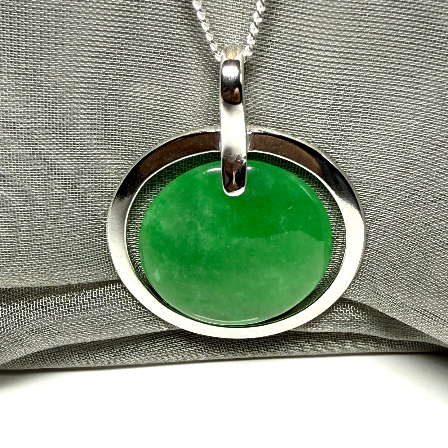 Green pendant with silver circular frame on a gray fabric background
