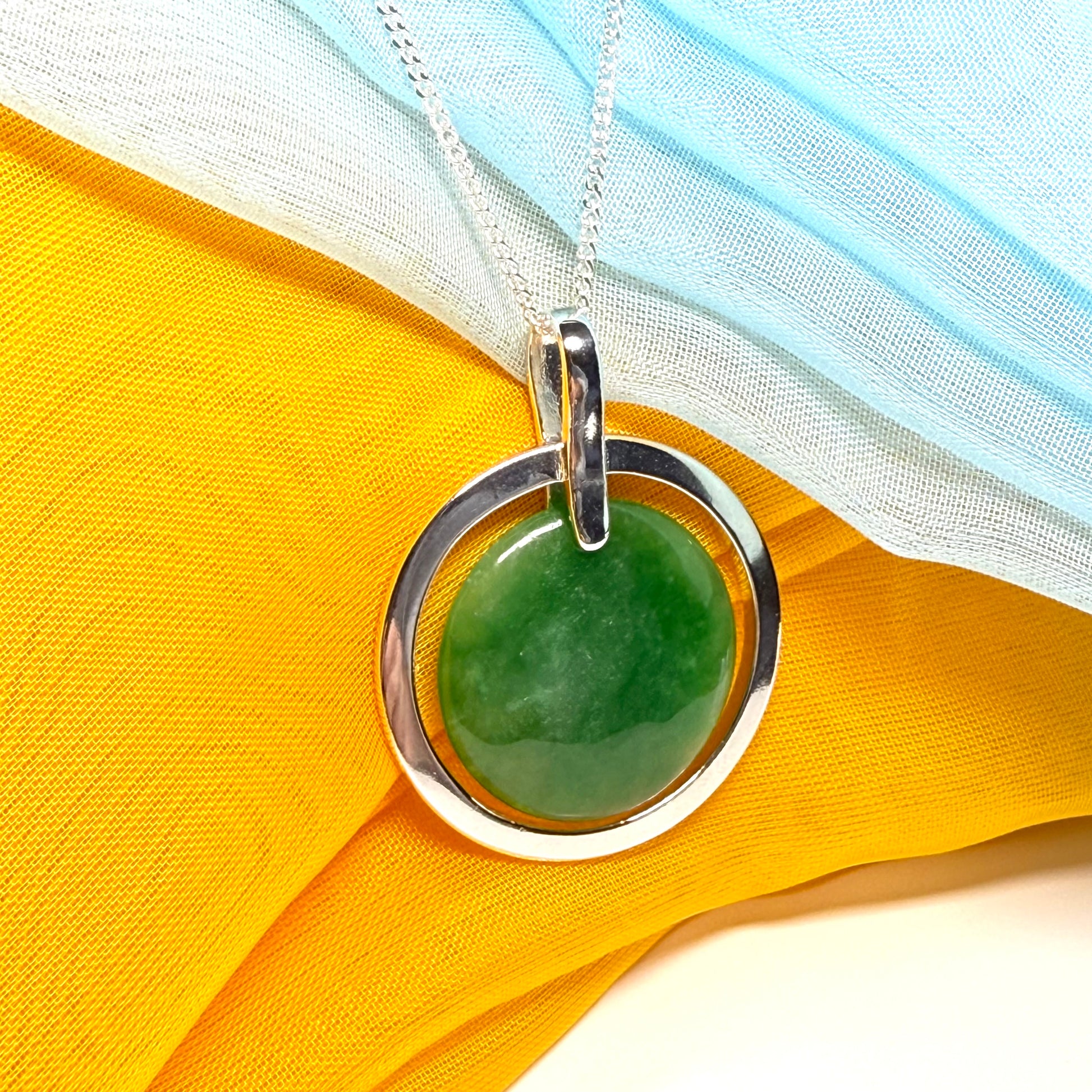 Green stone pendant with silver circle on a yellow fabric background