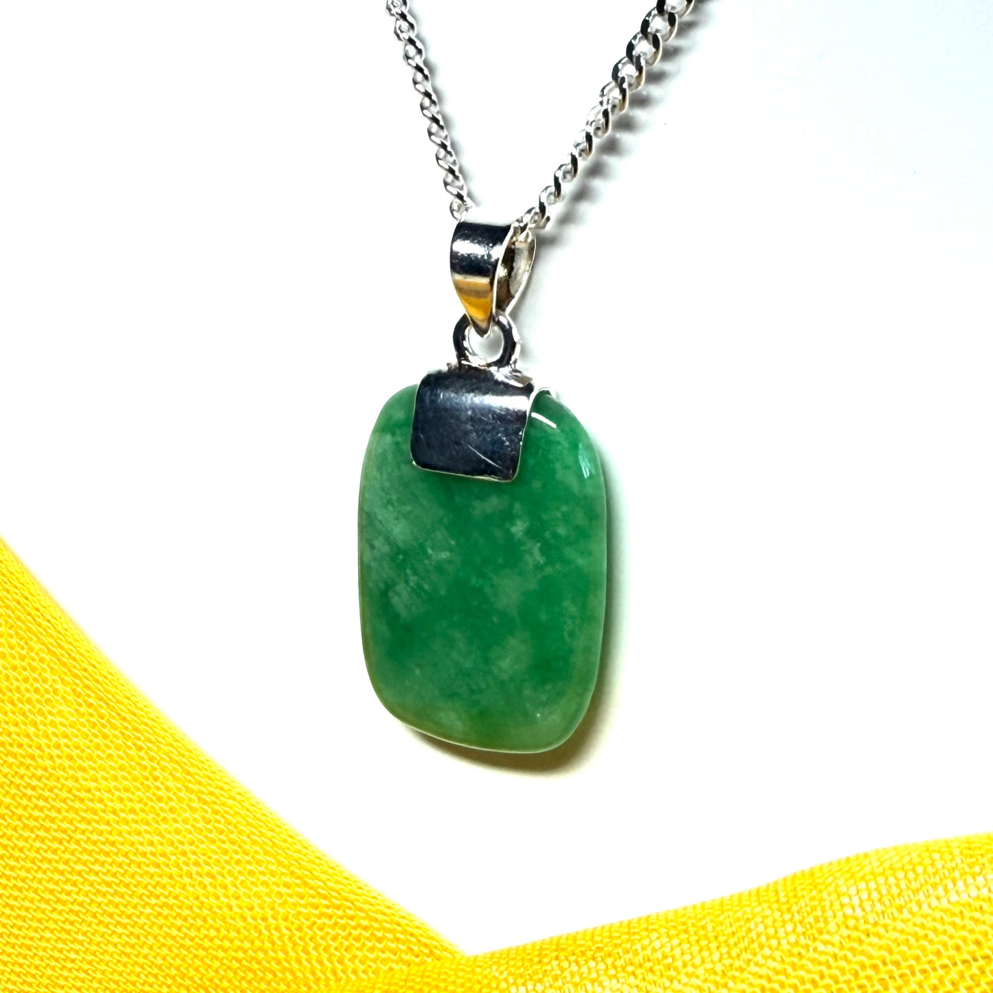 Green pendant on a silver chain against a yellow fabric background