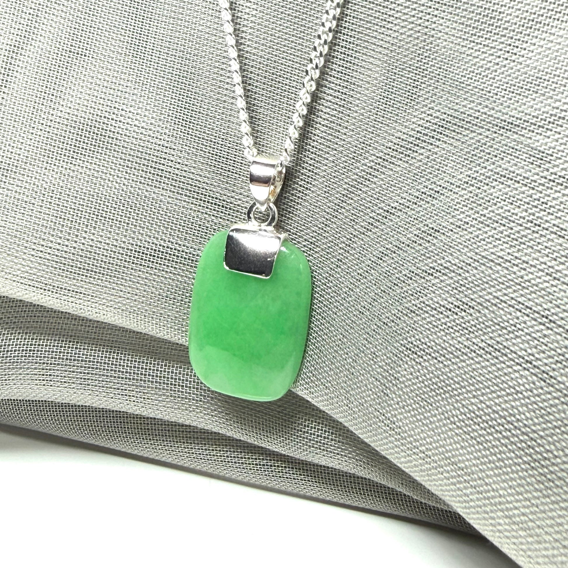 Green pendant necklace on a silver chain against a gray fabric background