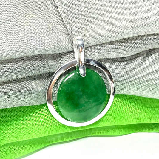 Green real jade pendant with silver circle on a green fabric background