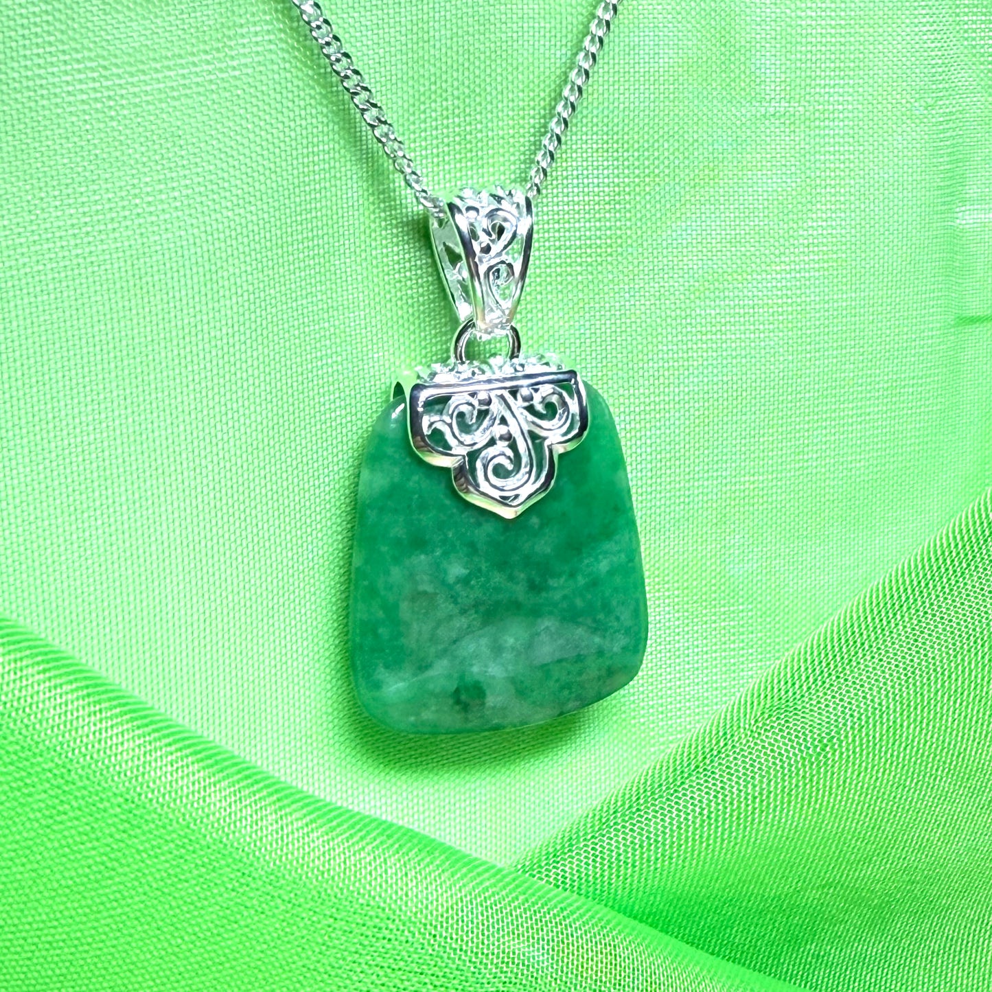 Green pendant with silver chain on a green fabric background