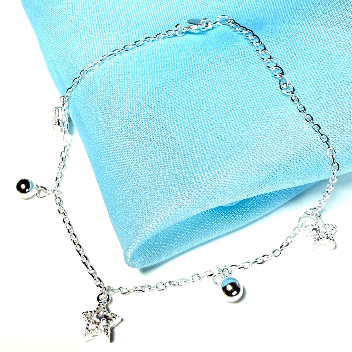 Silver bracelet with star and round charm on a light blue fabric background
