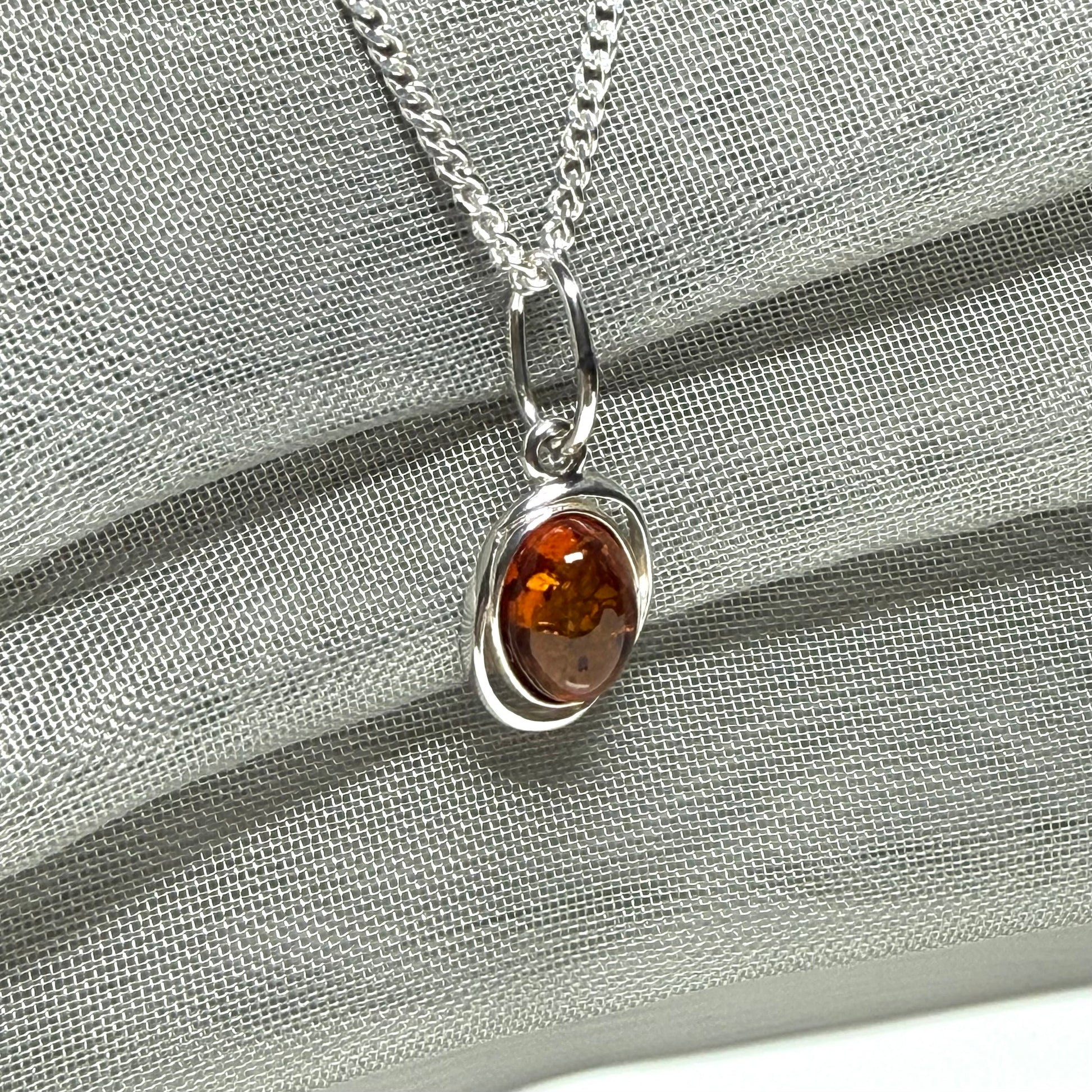 Orange real amber oval sterling silver necklace with a swirl set open pierced pendant