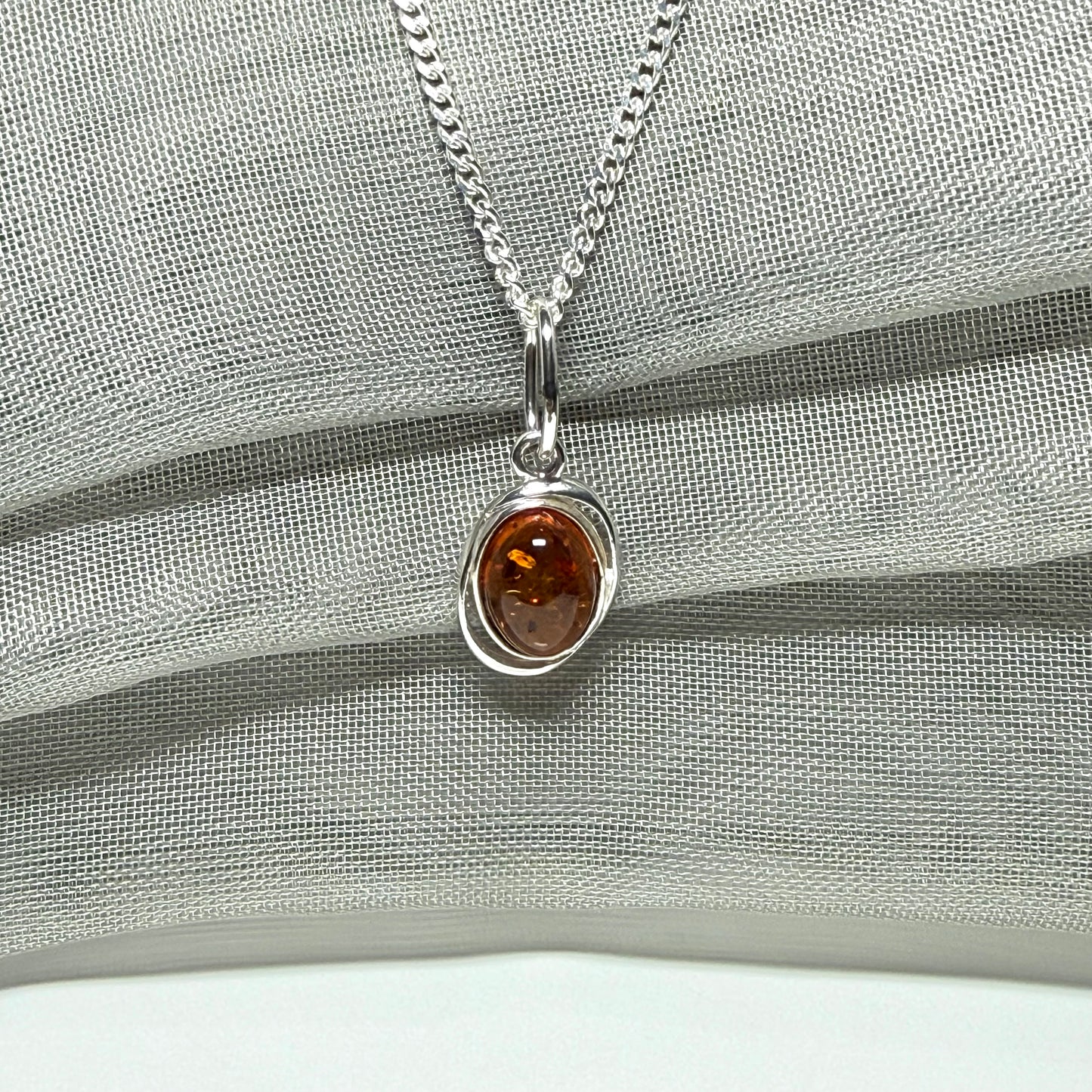 Orange real amber oval sterling silver necklace with a swirl set open pierced pendant