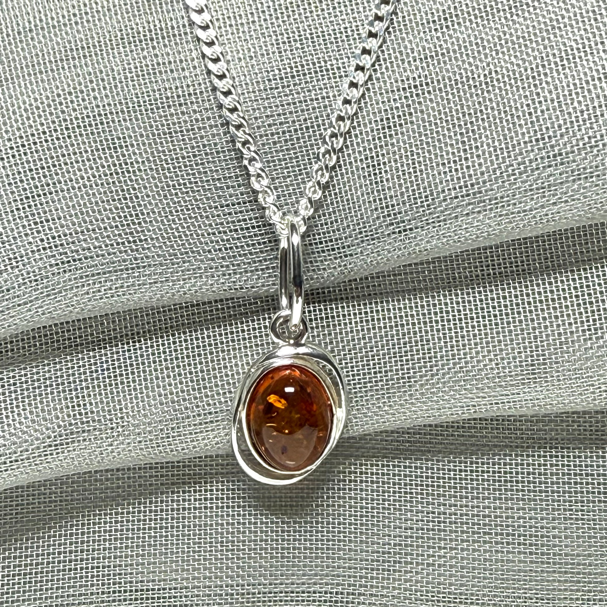 Orange real amber oval sterling silver necklace with a swirl set open pierced pendant