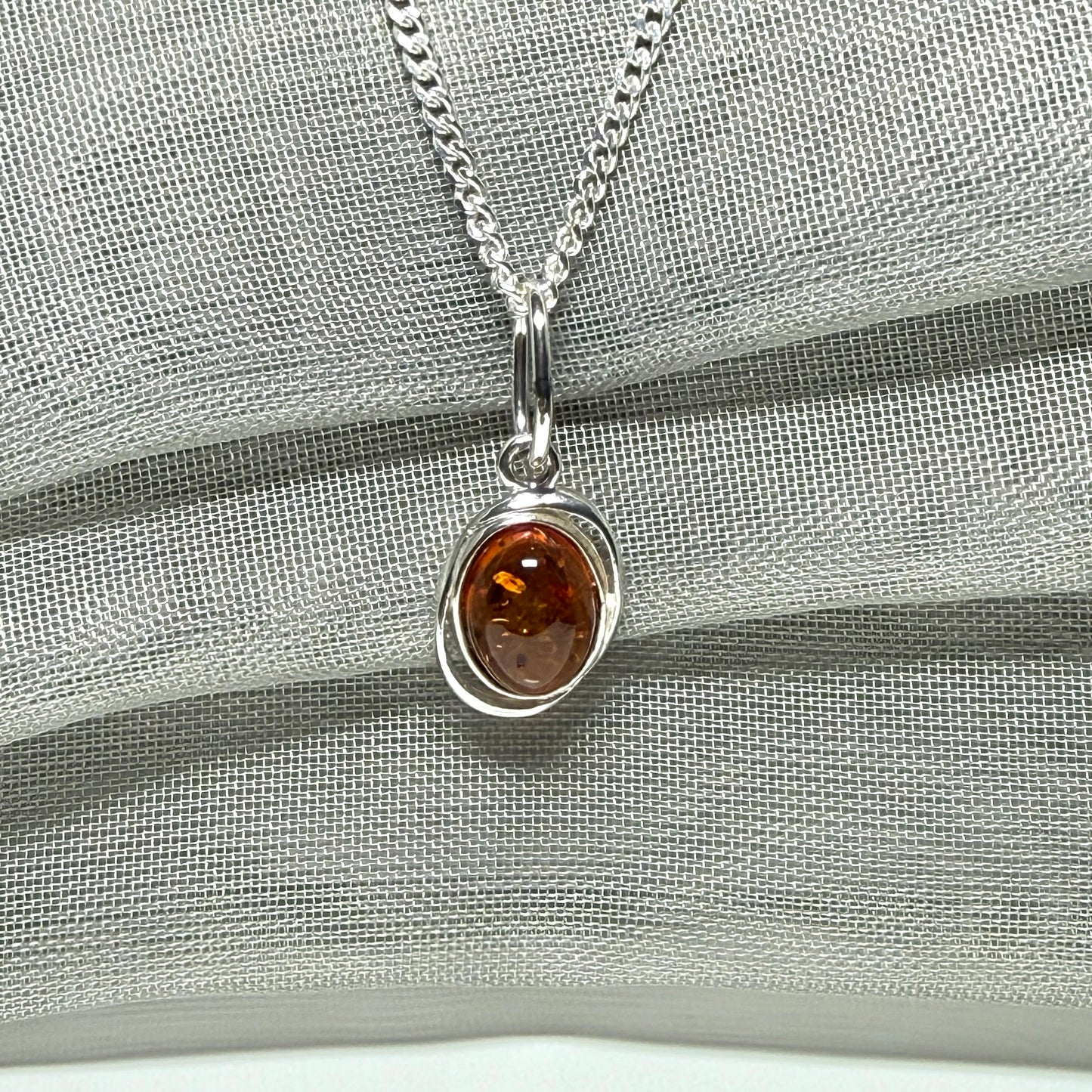 Orange real amber oval sterling silver necklace with a swirl set open pierced pendant