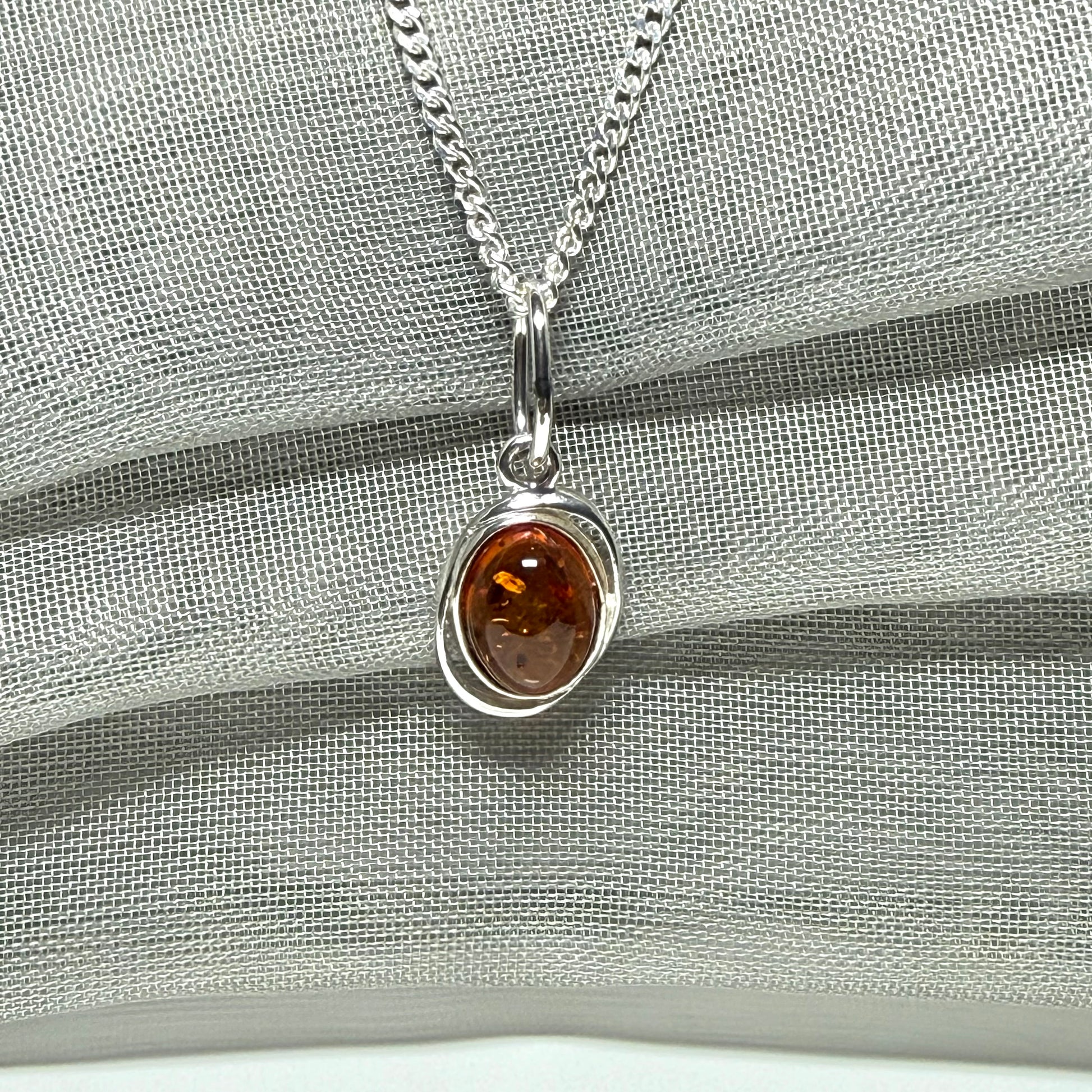 Orange real amber oval sterling silver necklace with a swirl set open pierced pendant
