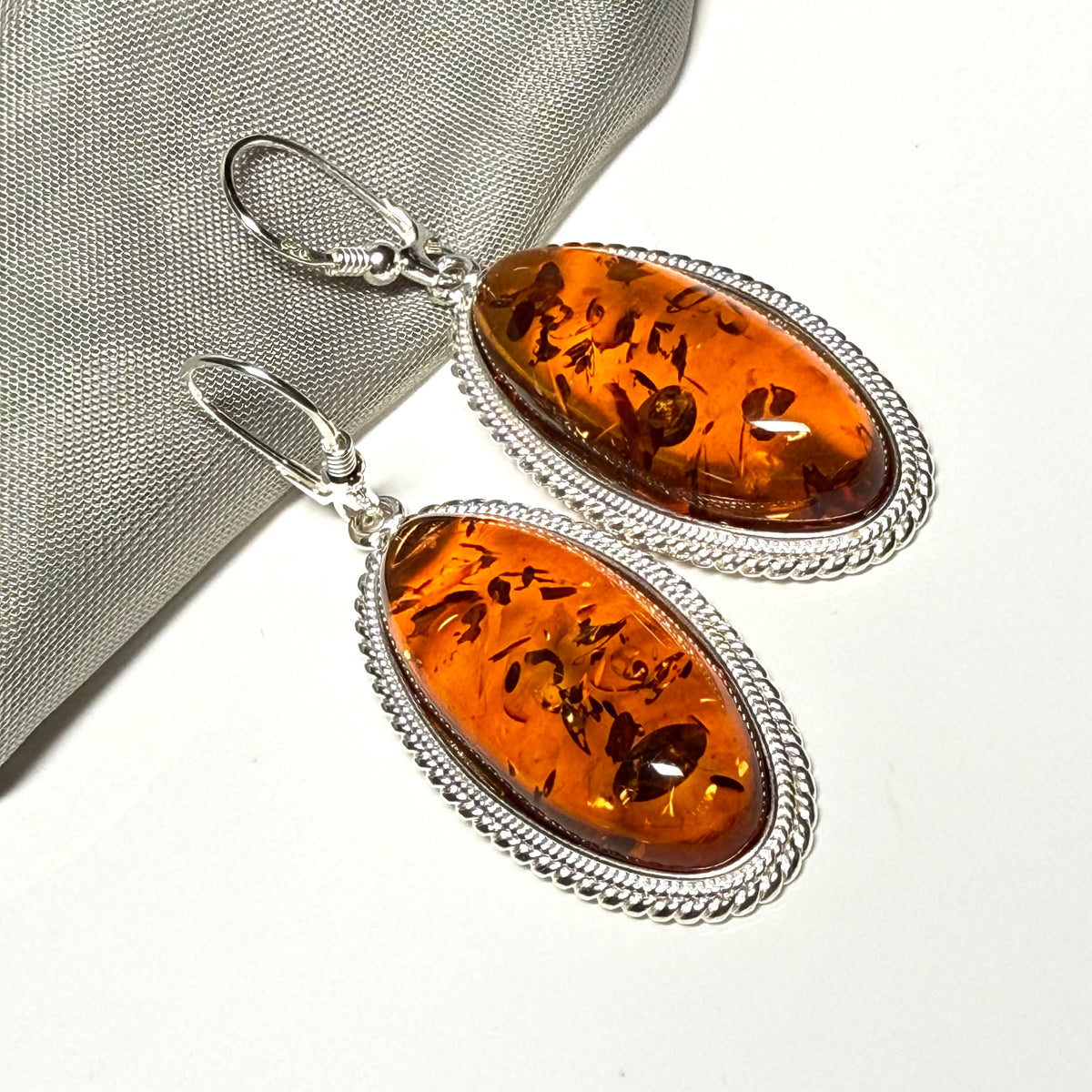 A pair of real amber drop earrings an oval shape rope edged sterling silver continental wired fittings