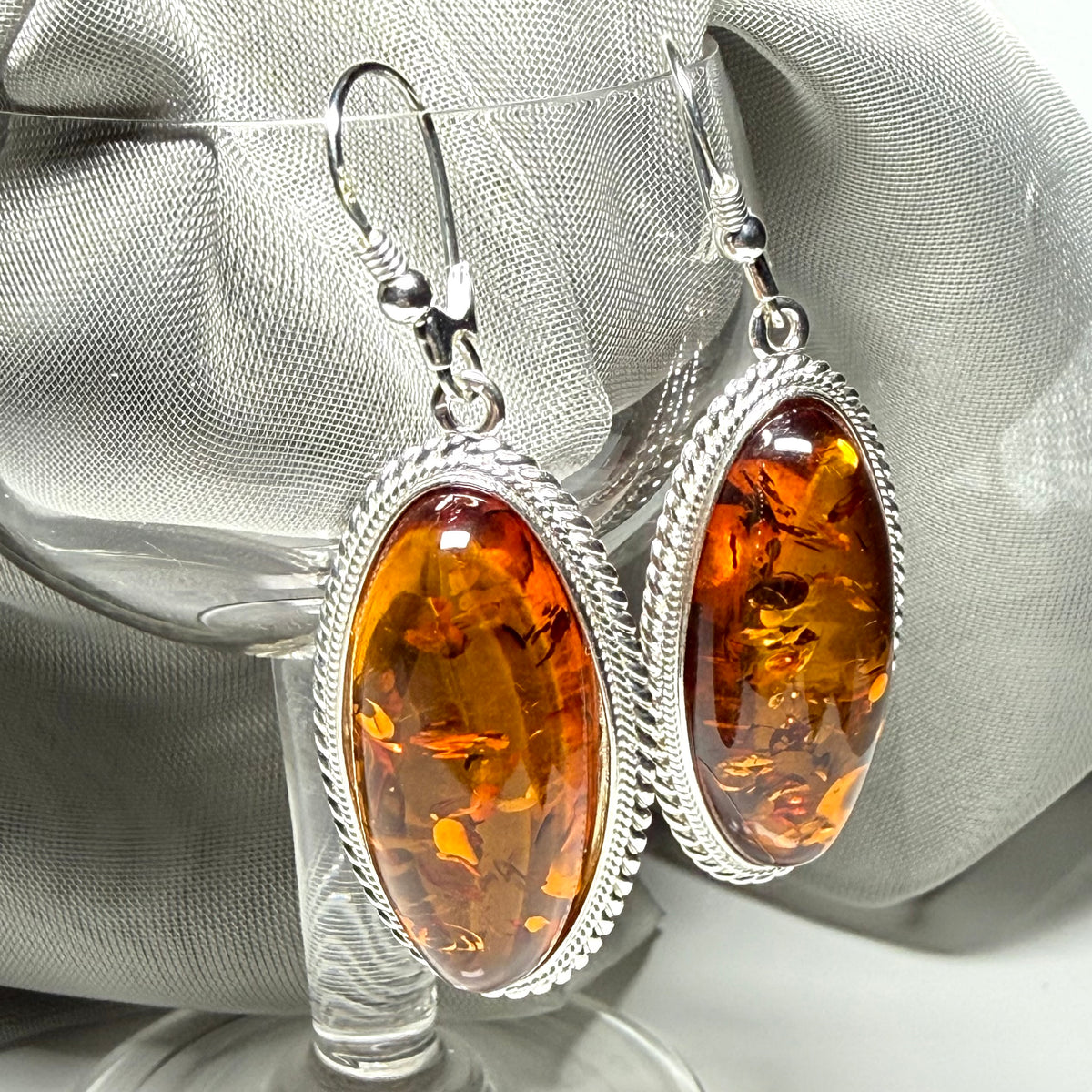 A pair of real amber drop earrings an oval shape rope edged sterling silver continental wired fittings
