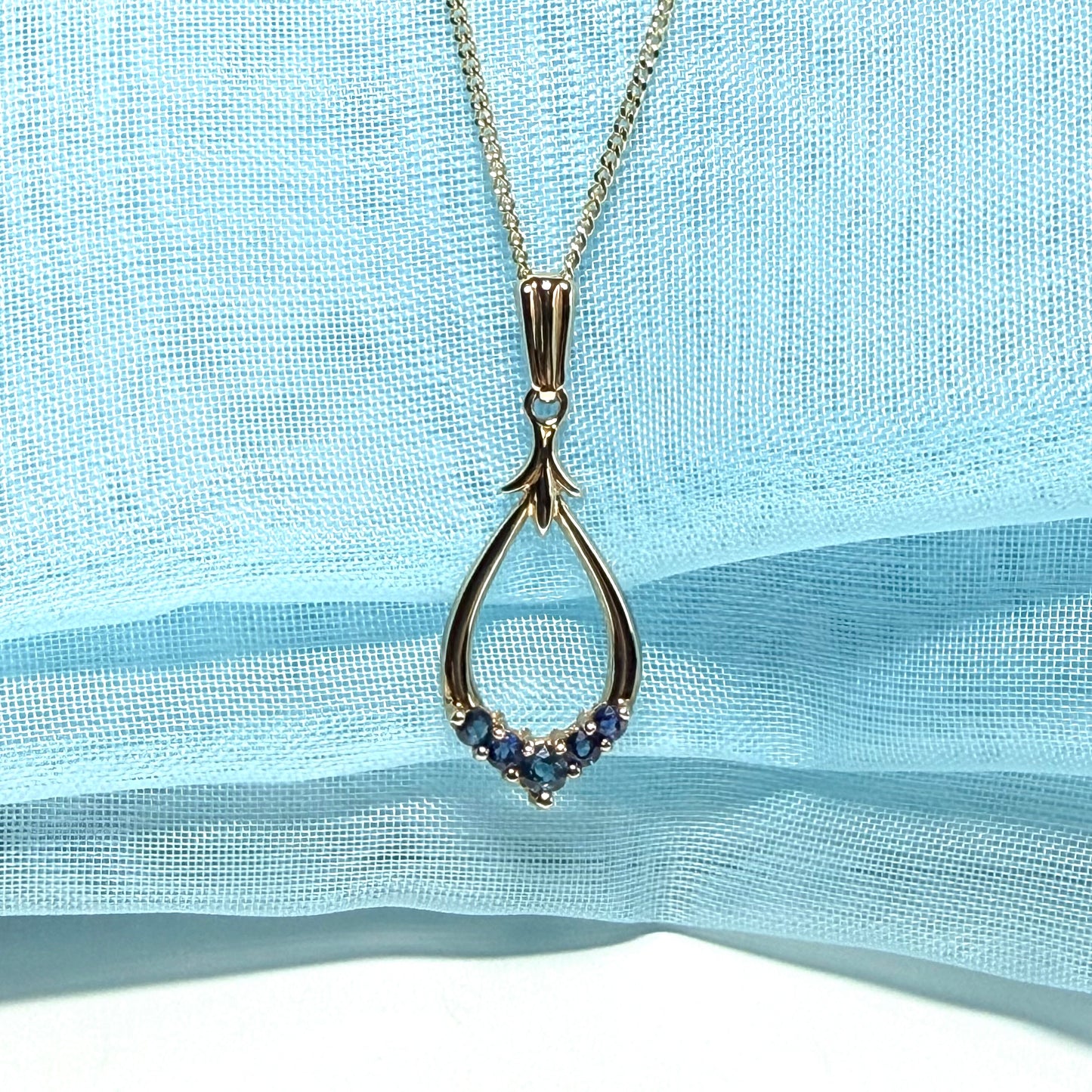 Teardrop-shaped pendant with small stones on a light blue fabric background