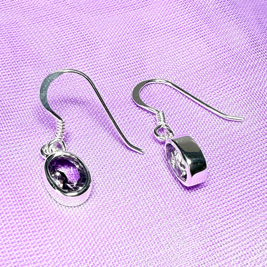 Silver earrings with purple gemstone on a purple fabric background