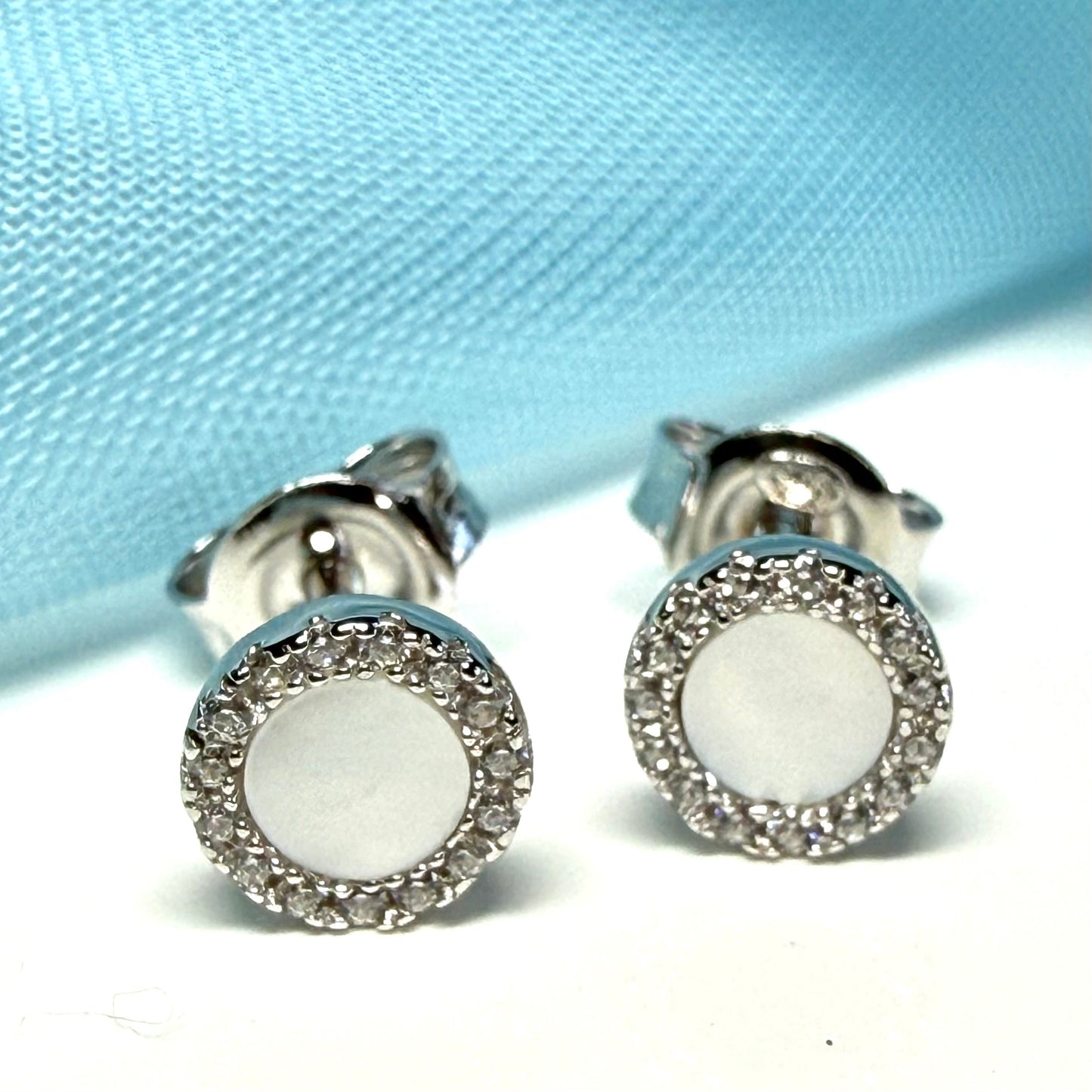 Silver earrings with white round stones on a light blue fabric background