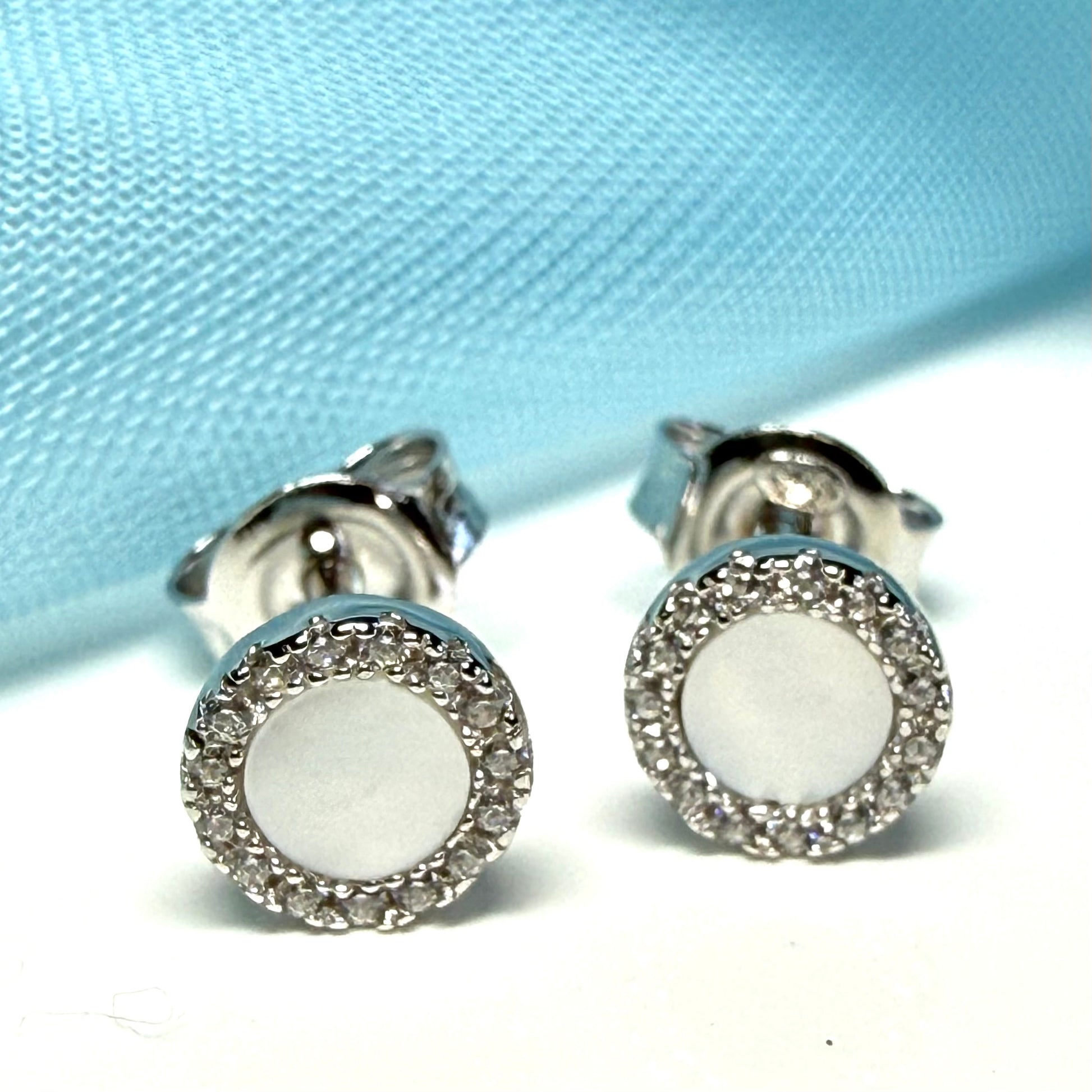 Silver earrings with white round stones on a light blue fabric background