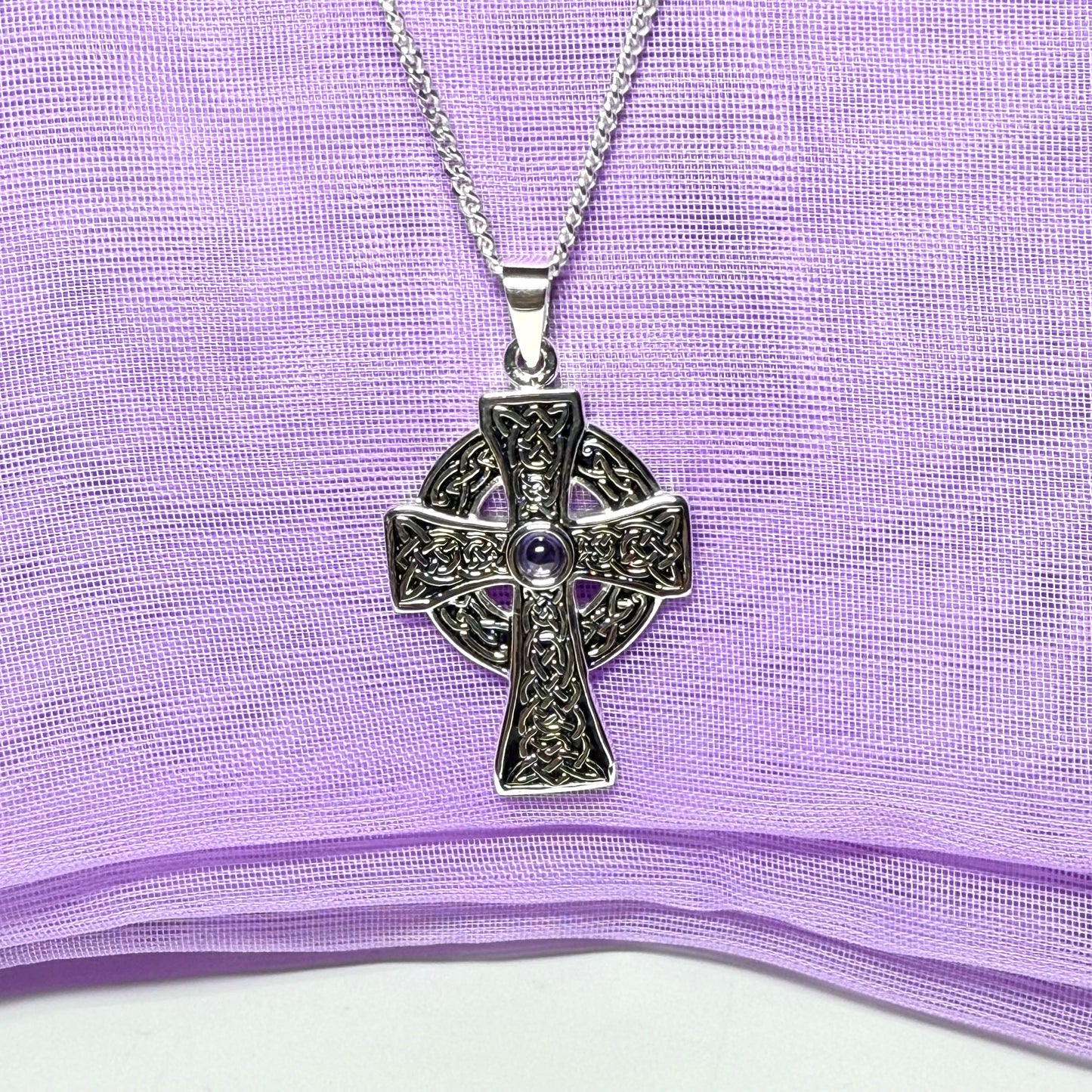 Silver Celtic cross necklace on a purple fabric background