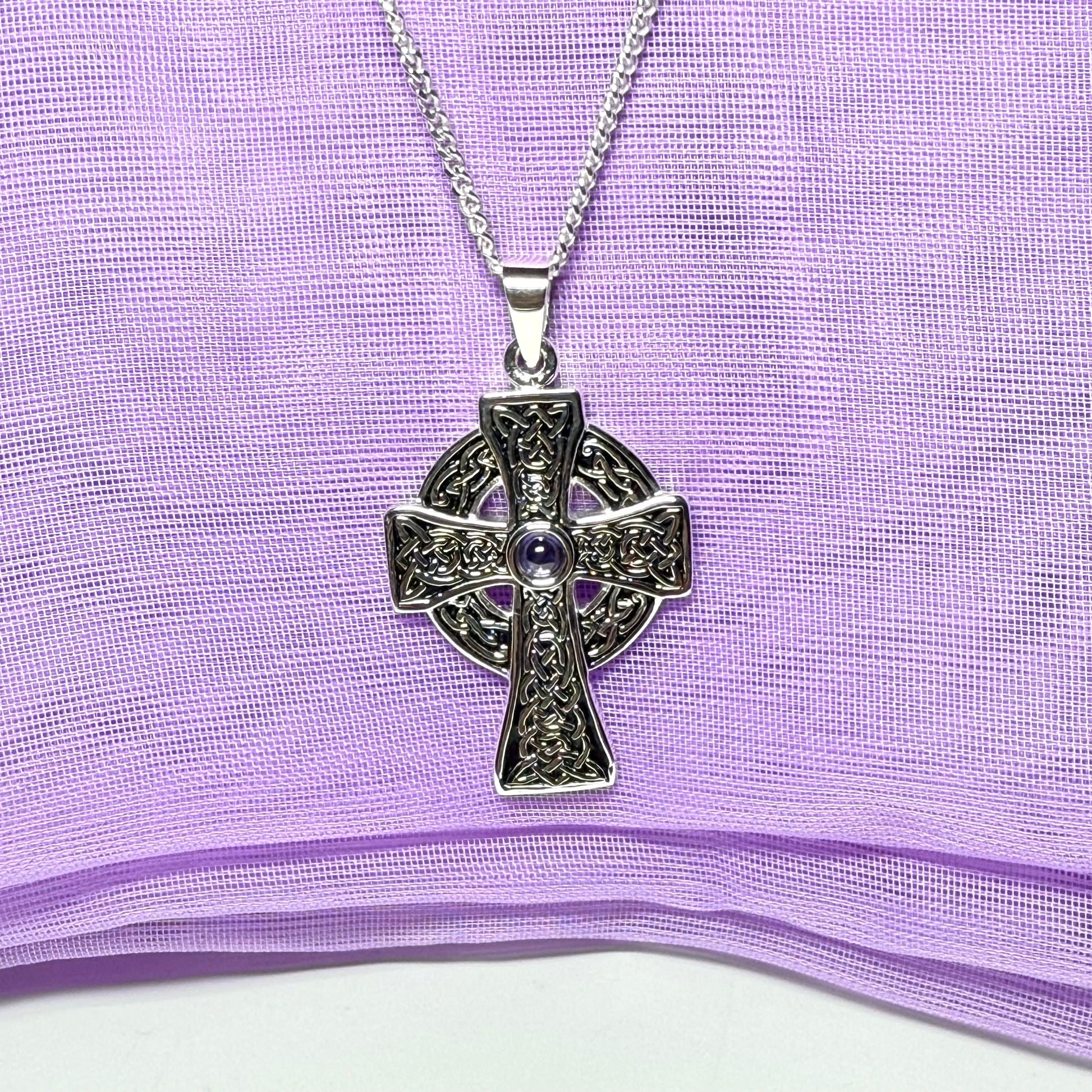Silver Celtic cross necklace on a purple fabric background