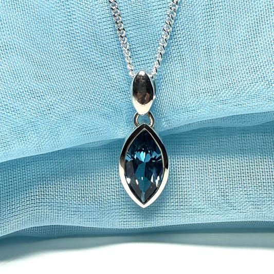 Silver necklace with a blue teardrop pendant on a light blue fabric background