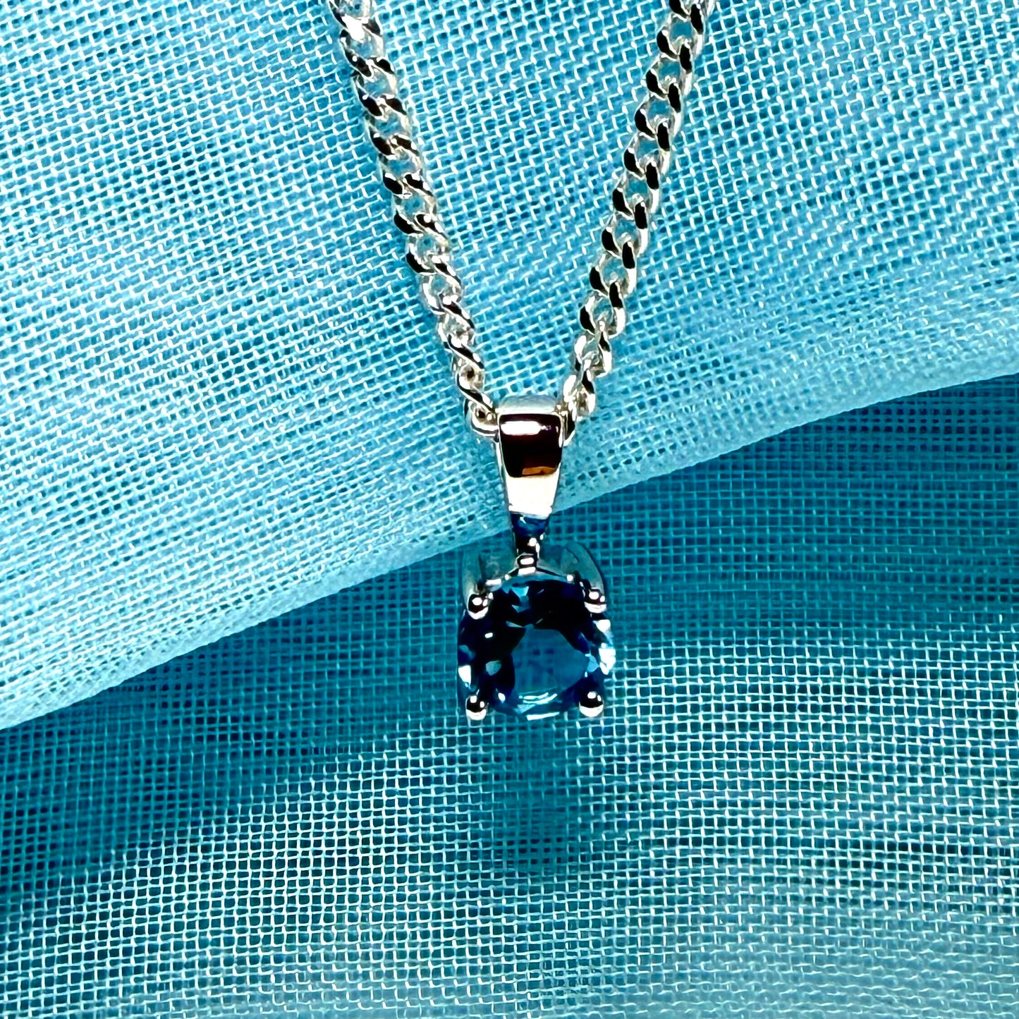 Silver necklace with a blue pendant on a blue textured background