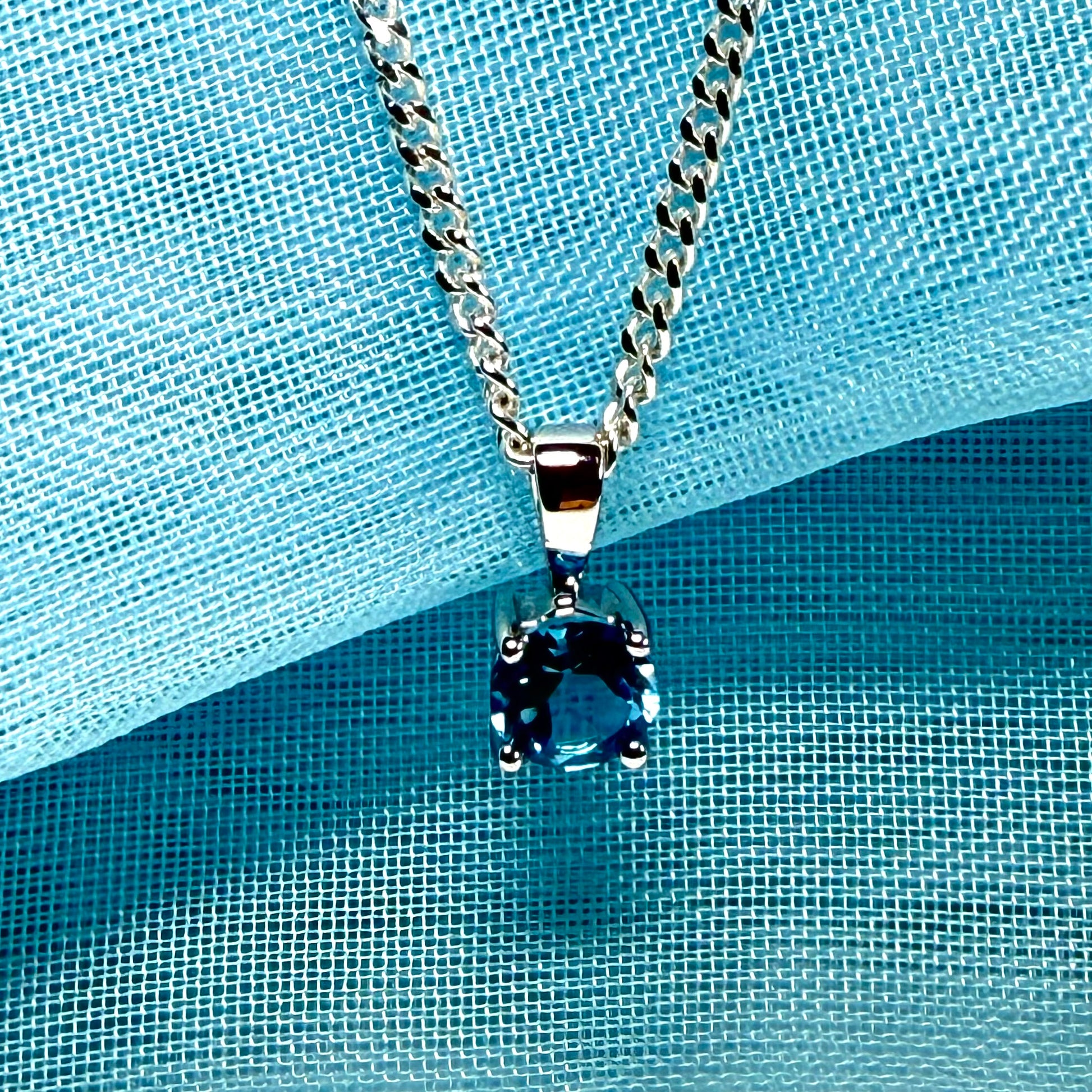 Silver necklace with a blue pendant on a blue textured background