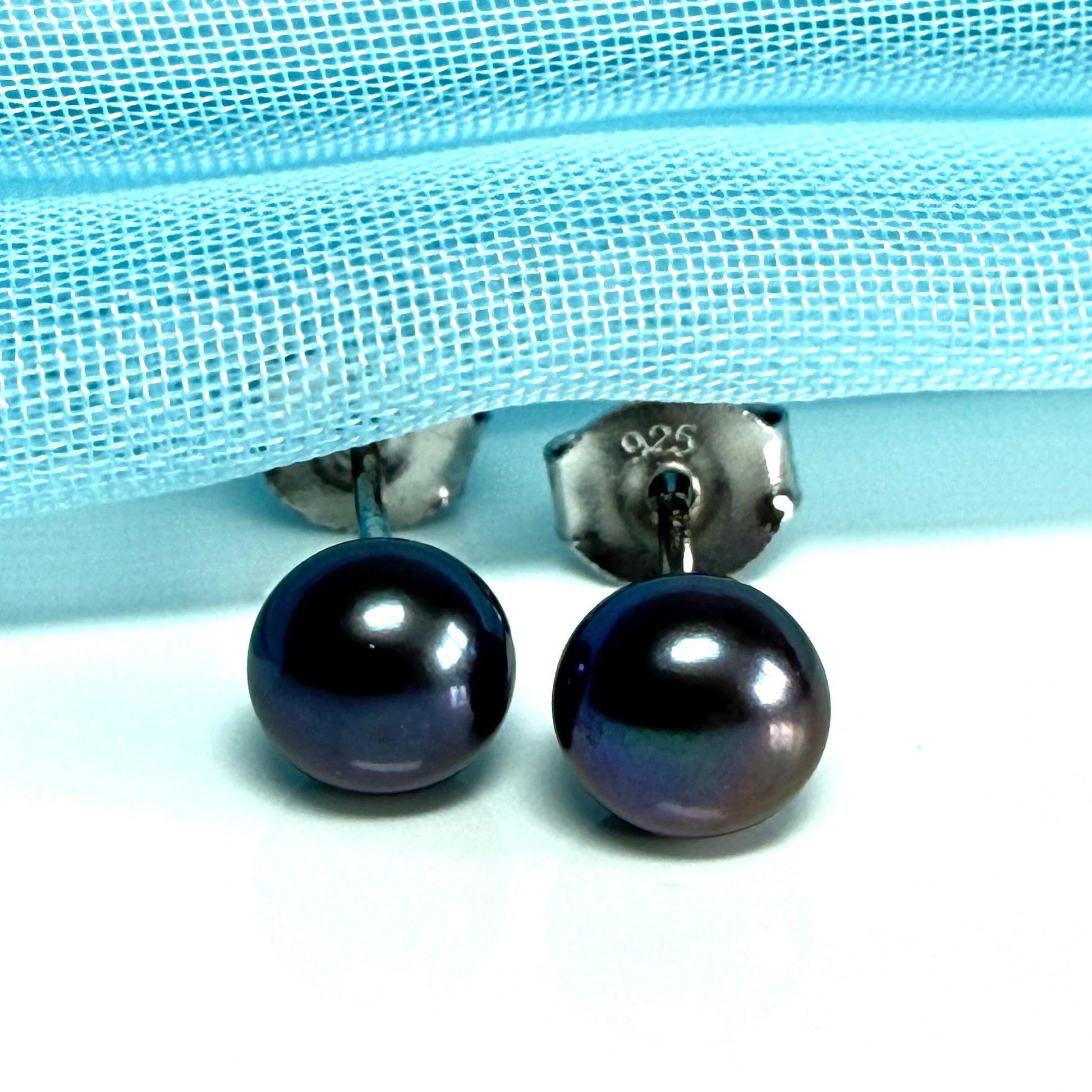 Pair of black pearl earrings on a light blue fabric background