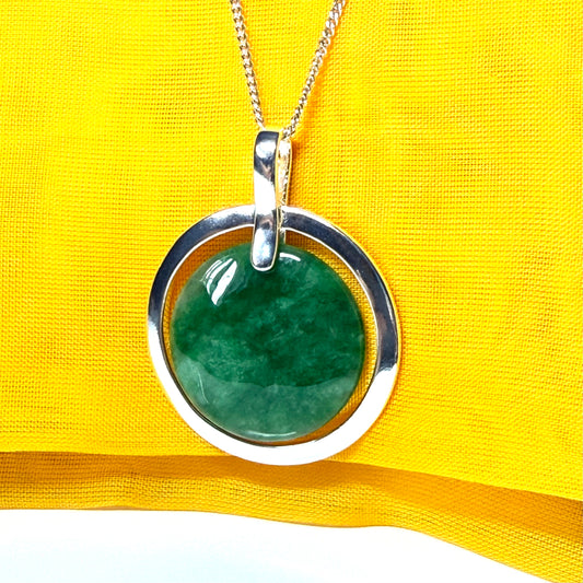 Dark green real jade stone pendant with silver frame on a yellow fabric background