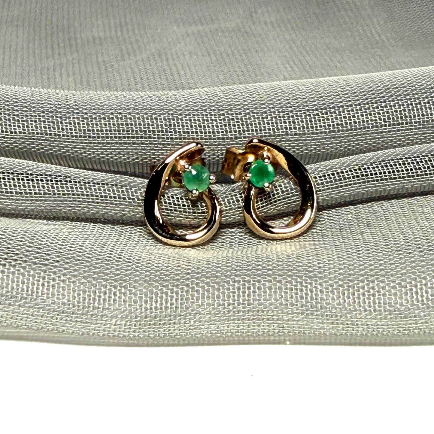 Gold hoop earrings with green gemstones on a gray fabric background