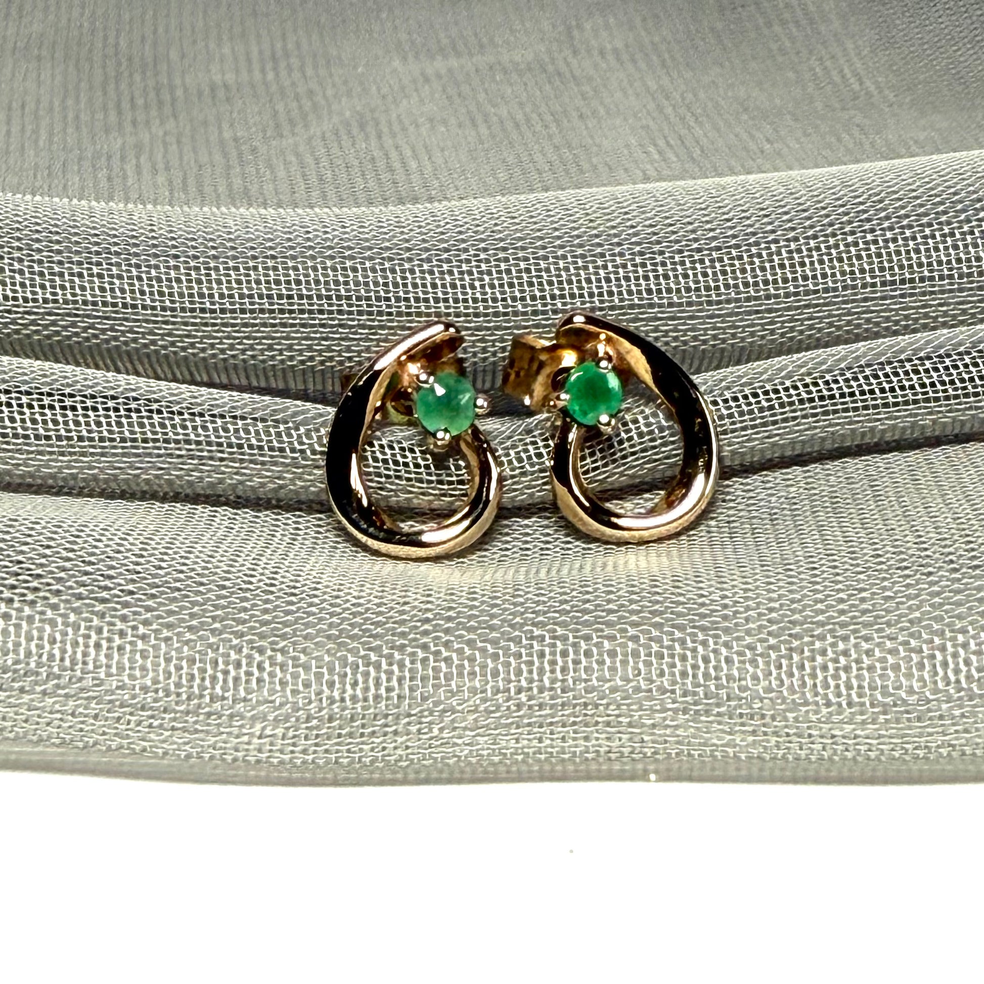 Gold hoop earrings with green gemstones on a gray fabric background