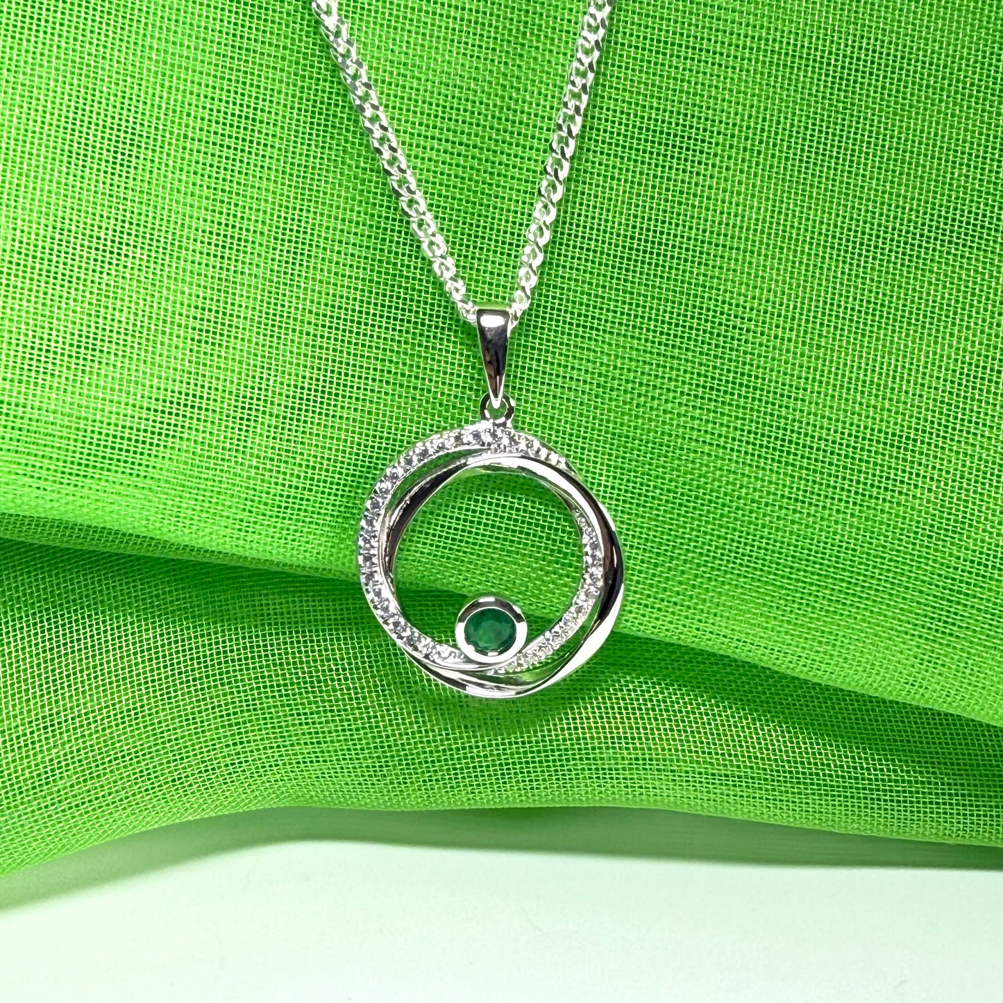 Silver necklace with a circular pendant on a green fabric background