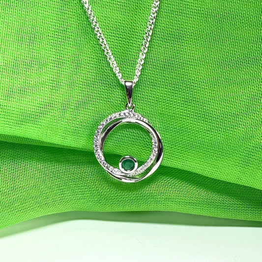 Silver necklace with a circular pendant on a green fabric background