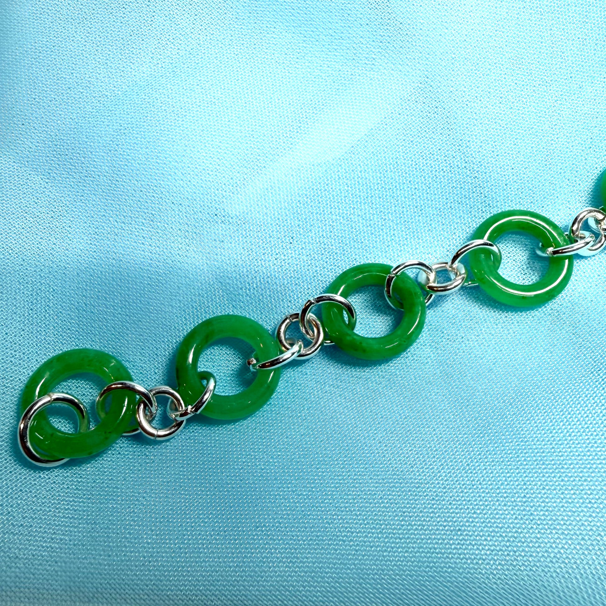 Green jade chain bracelet on a light blue fabric background