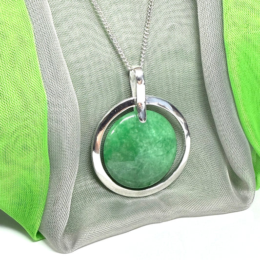 Real green jade necklace with a green pendant and silver circle on a green and gray fabric background