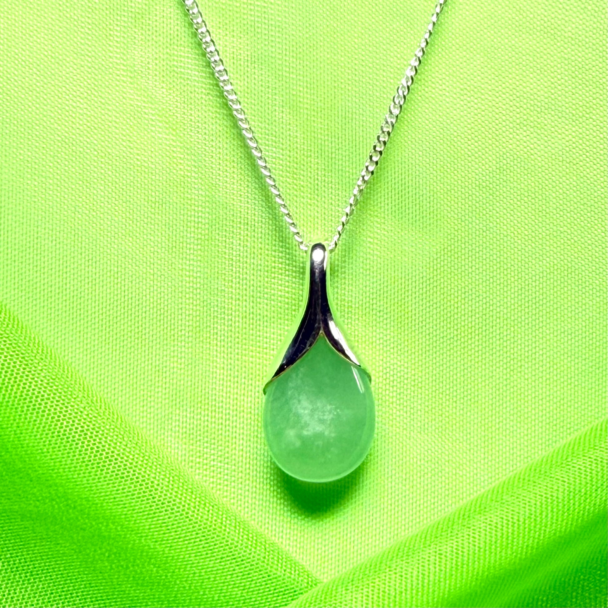 Necklace with a green teardrop pendant on a bright green fabric background