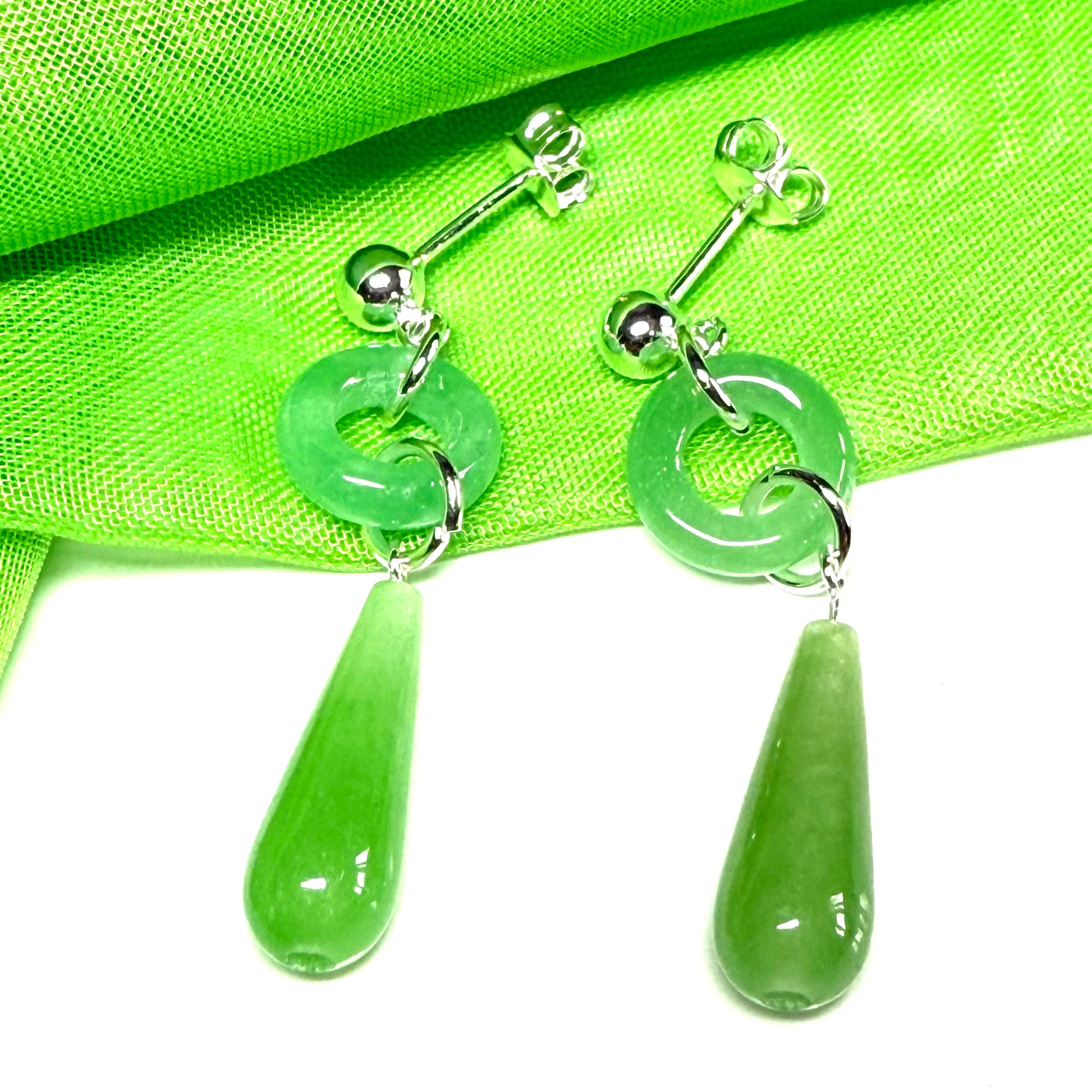 Real green jade teardrop earrings with silver loops on a green fabric background
