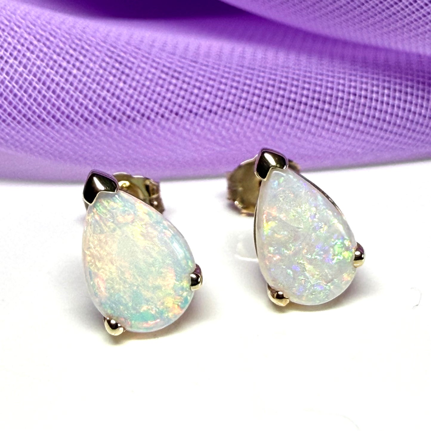Opal earrings on a white surface with a purple fabric background