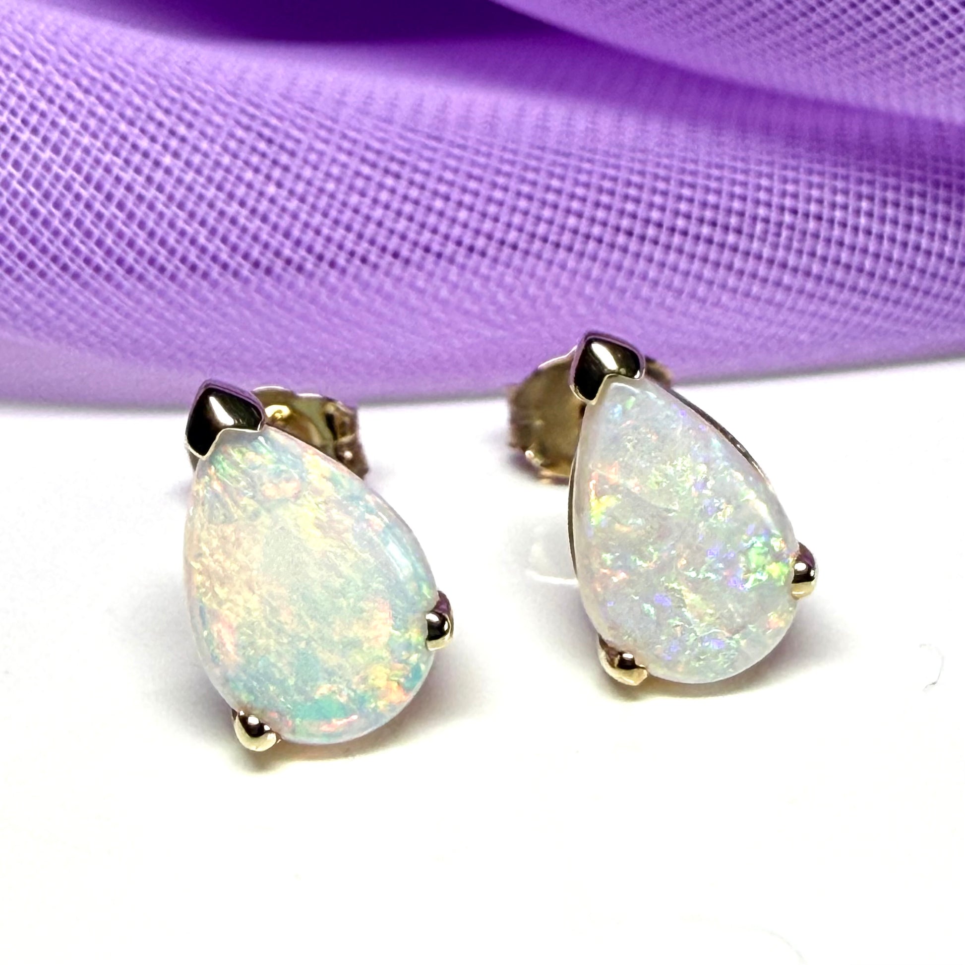 Opal earrings on a white surface with a purple fabric background