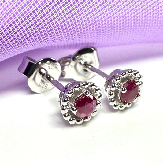 Silver earrings with red gemstones on a light purple background