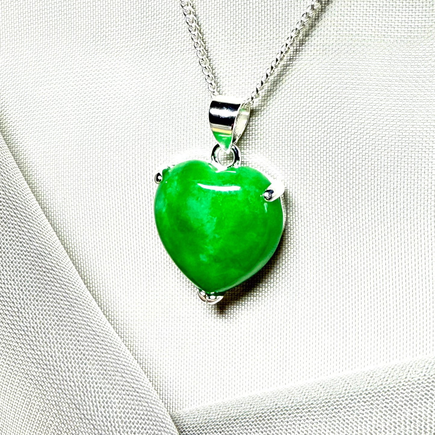 Green heart-shaped pendant on a silver chain against a light fabric background