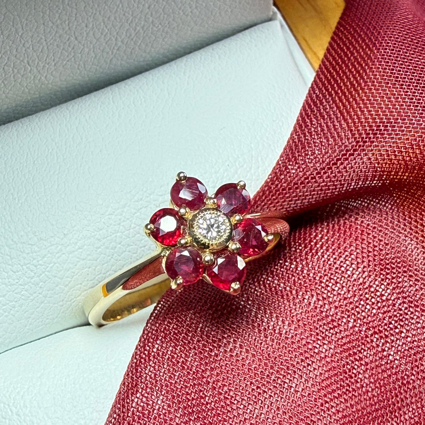 Gold ring with red gemstones and a diamond on a textured surface