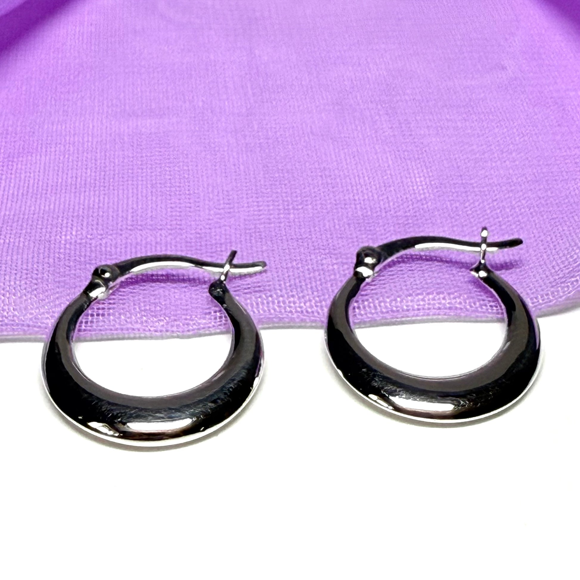 Black hoop earrings on a white surface with a purple fabric background