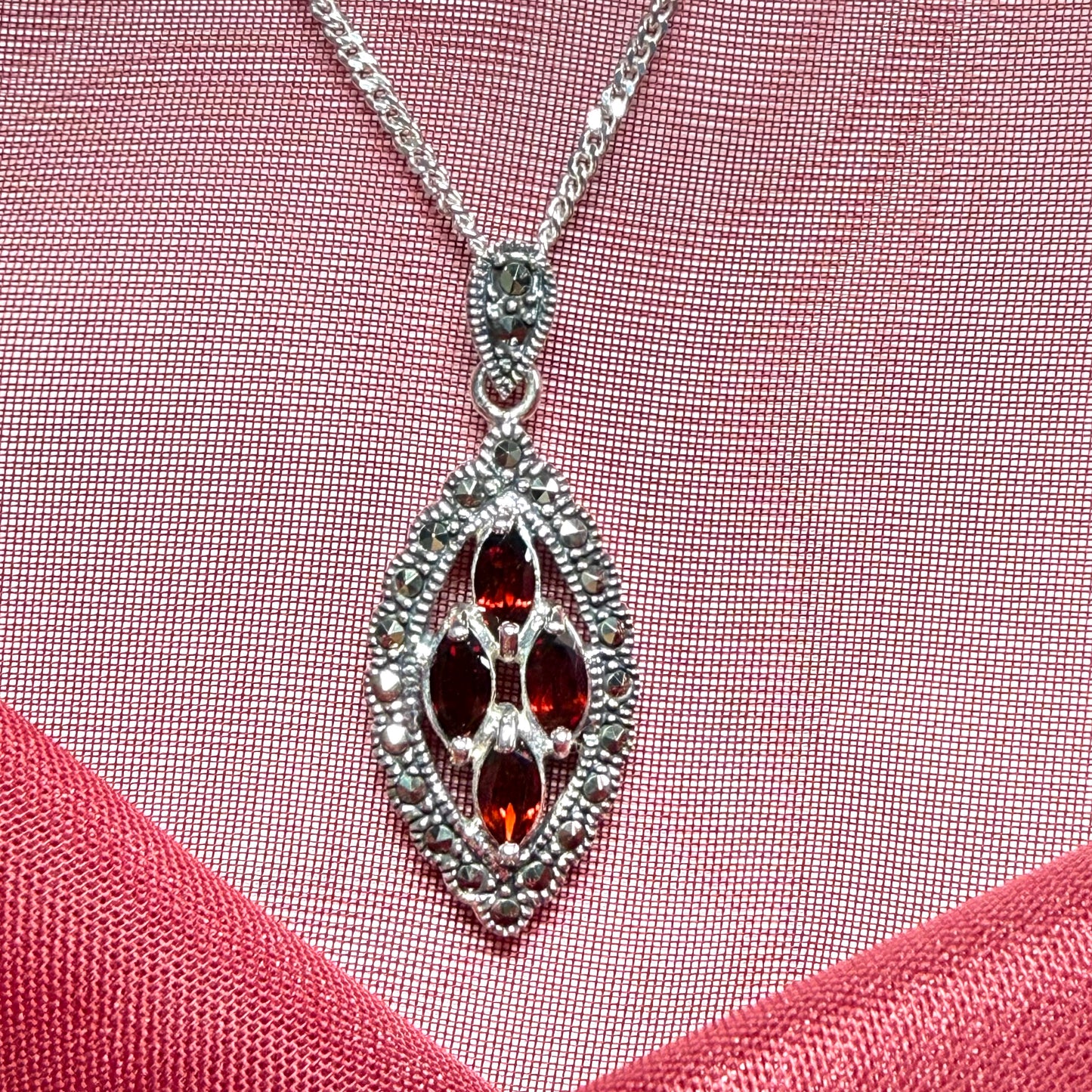 Silver necklace with a red gemstone pendant on a pink fabric background