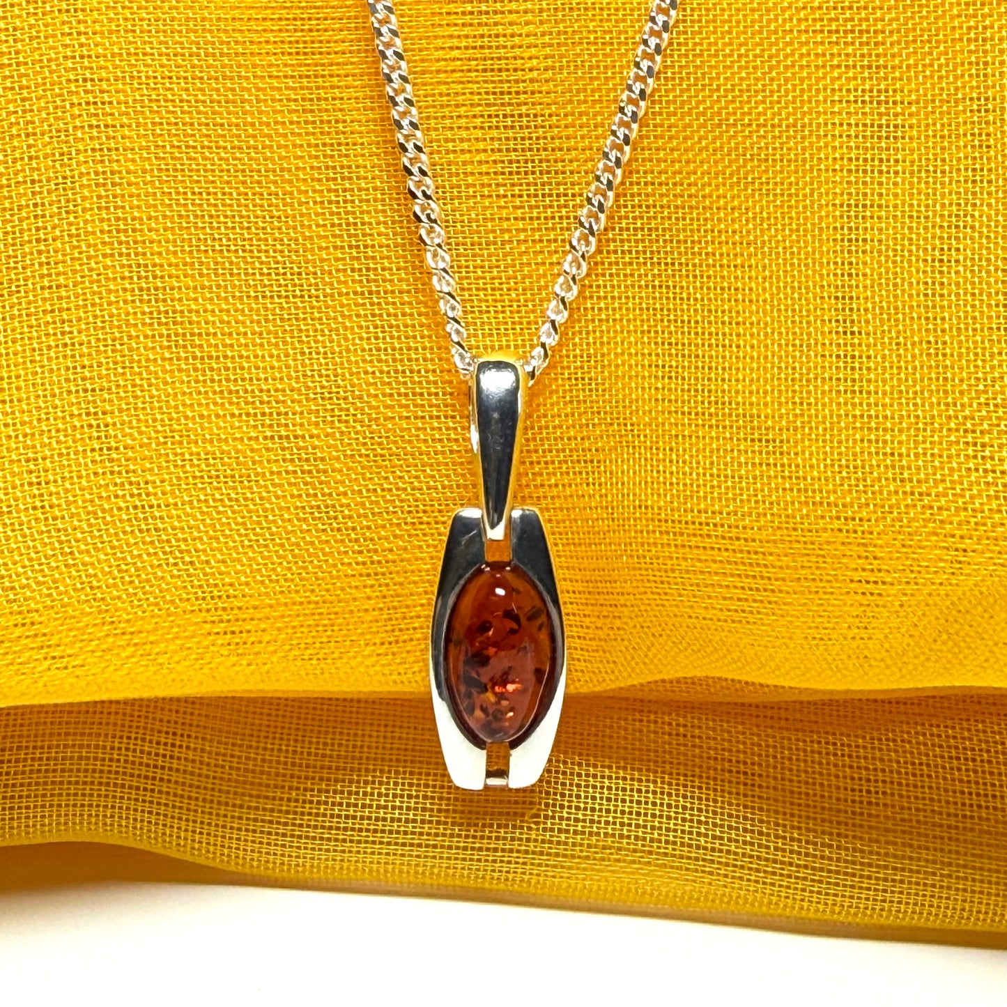 Silver pendant with amber stone on a yellow fabric background