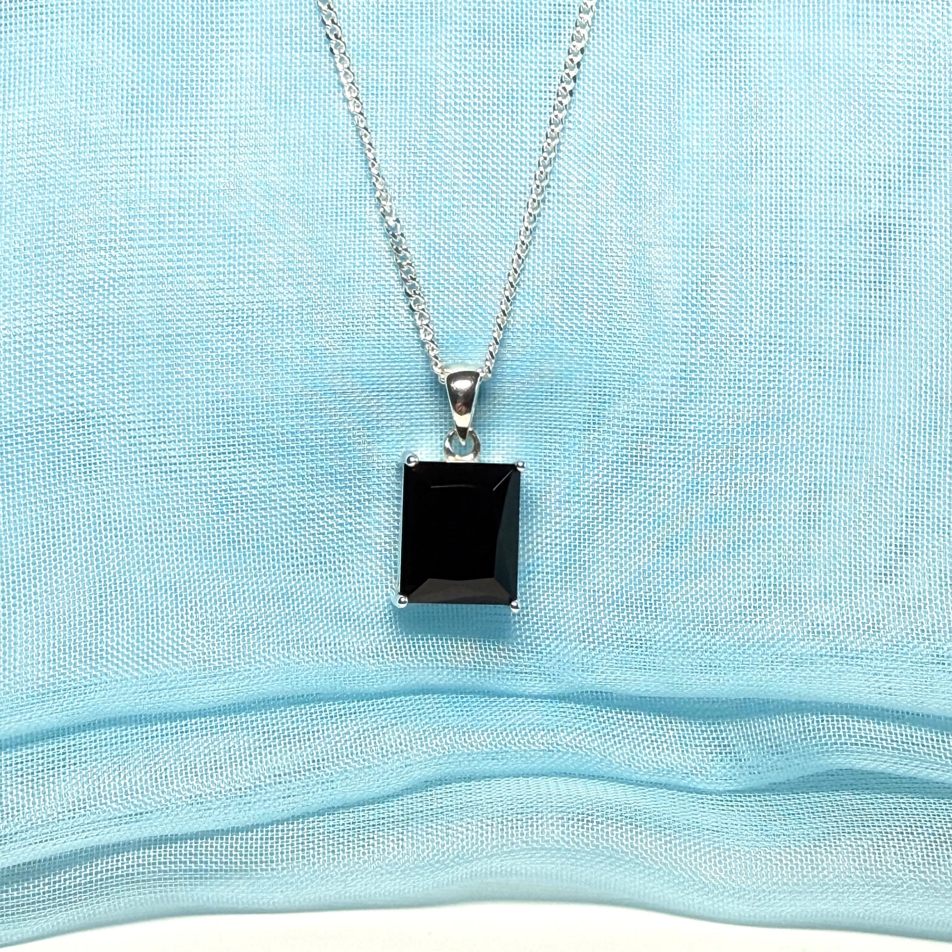 Black square pendant on a silver chain against a light blue fabric background