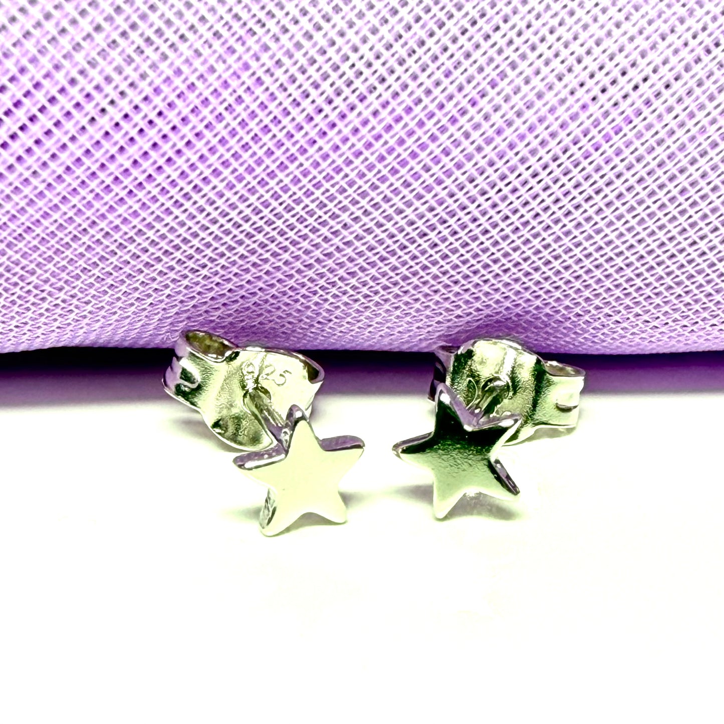 Star-shaped silver earrings on a purple and white checkered background