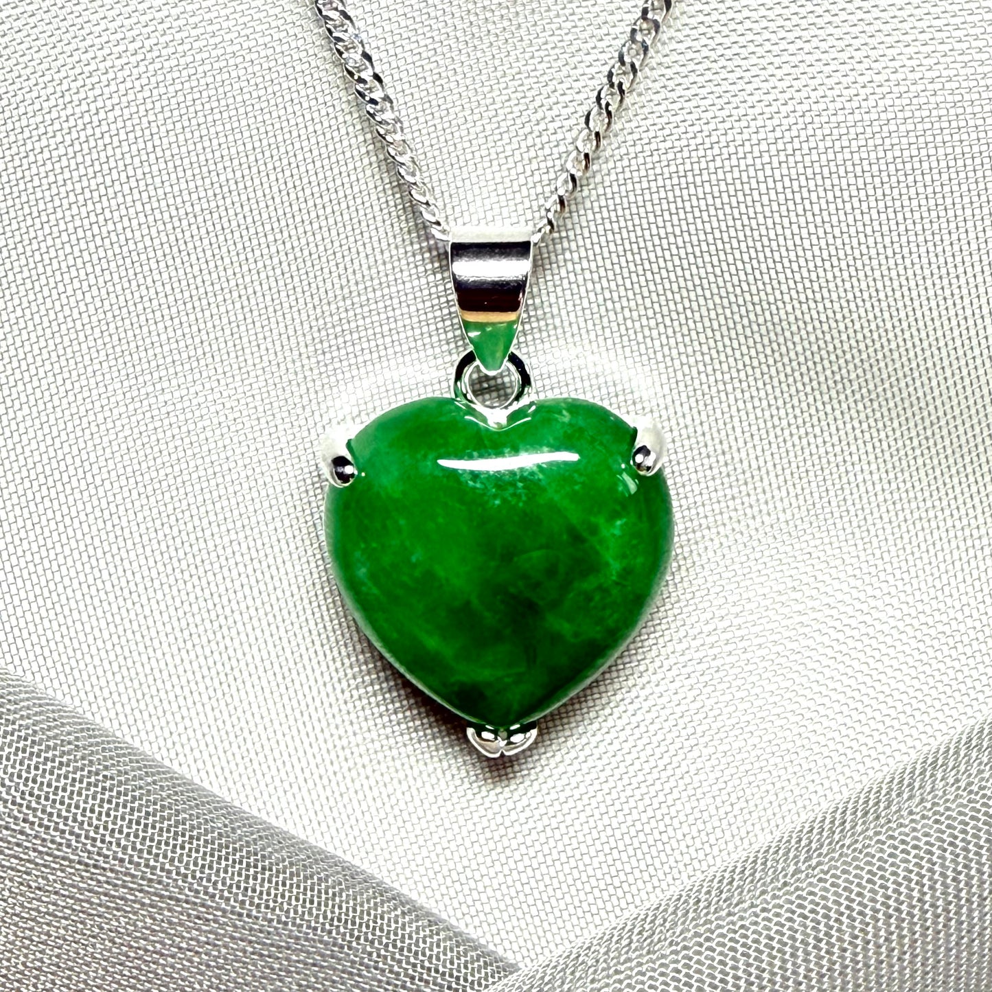 Green heart-shaped pendant on a silver chain against a gray fabric background