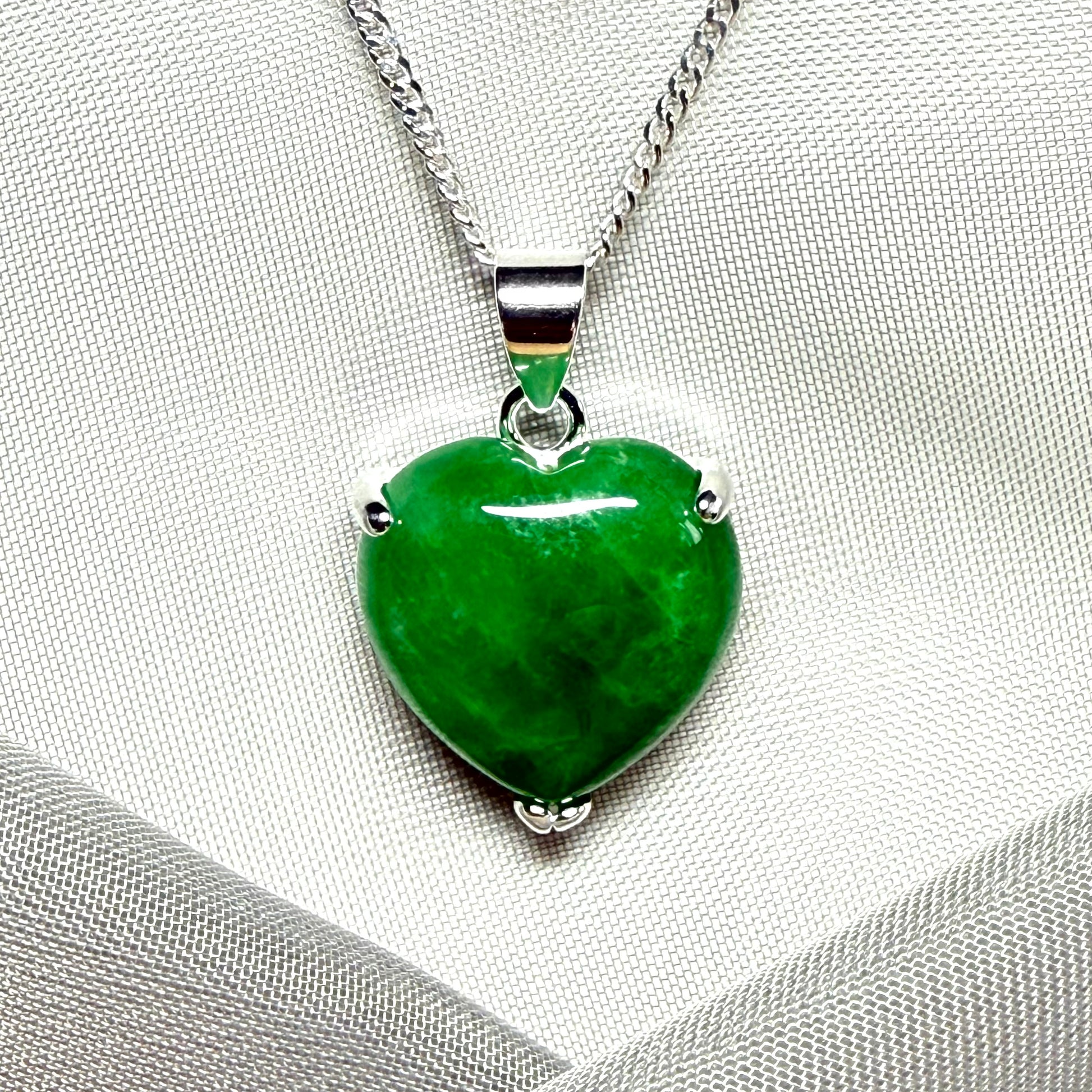 Green heart-shaped pendant on a silver chain against a gray fabric background