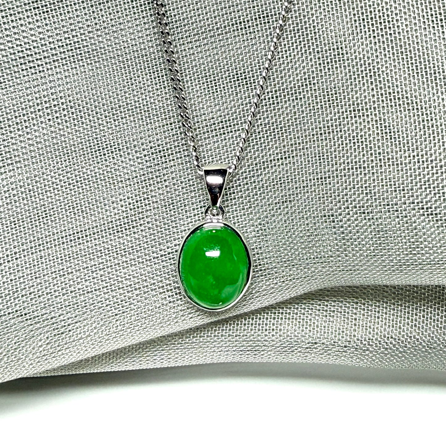 Green jade pendant on a silver chain against a gray fabric background