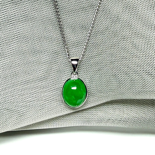Green jade pendant on a silver chain against a gray fabric background