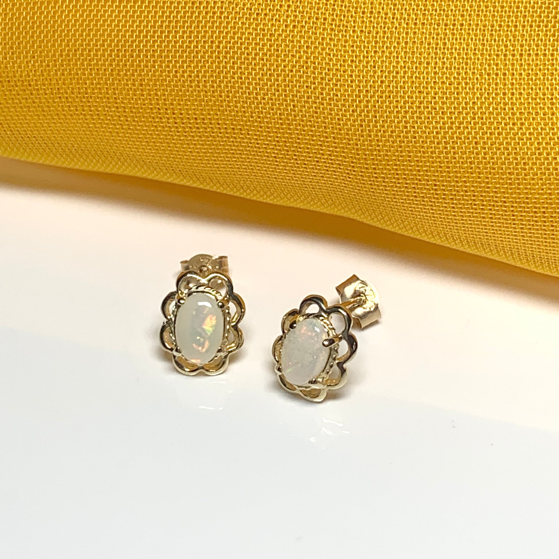 Yellow gold real opal oval stud earrings with a fancy scrolled edging