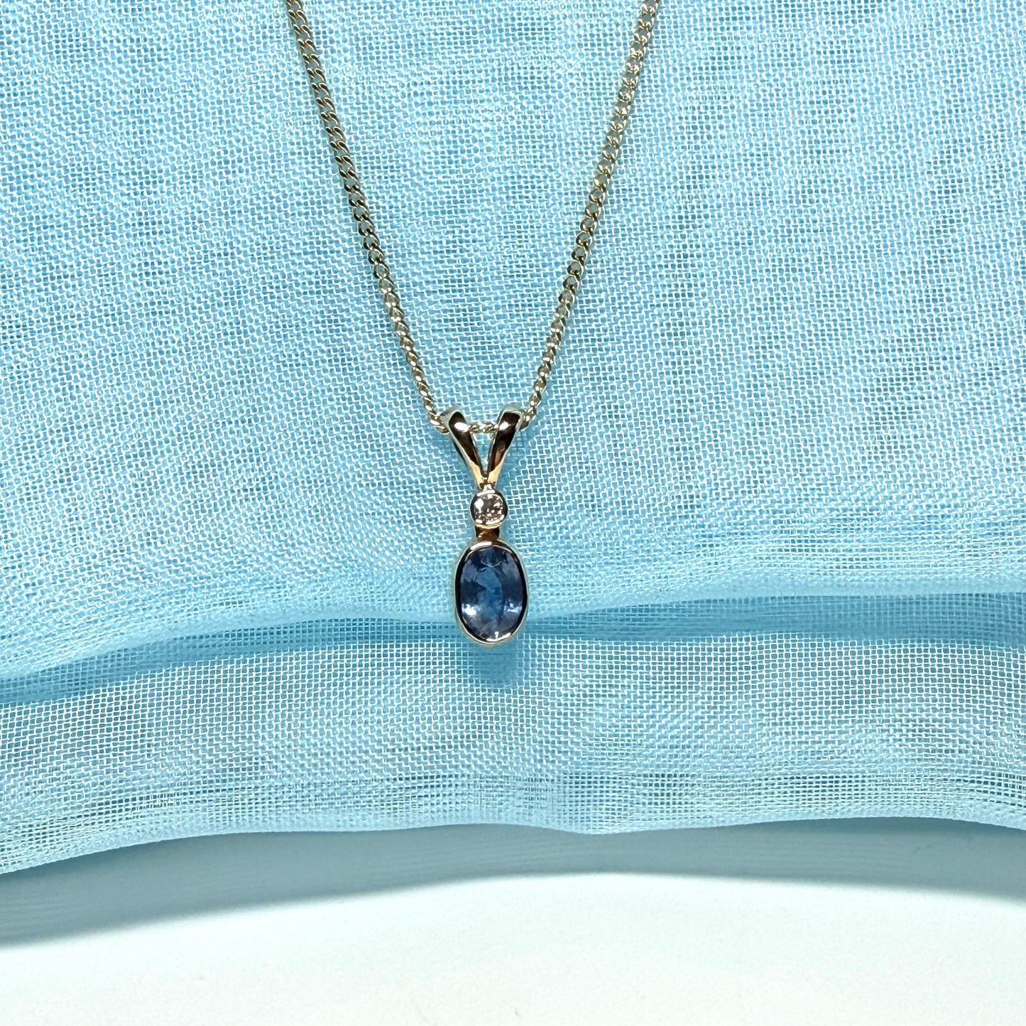 Gold necklace with a blue pendant on a light blue fabric background